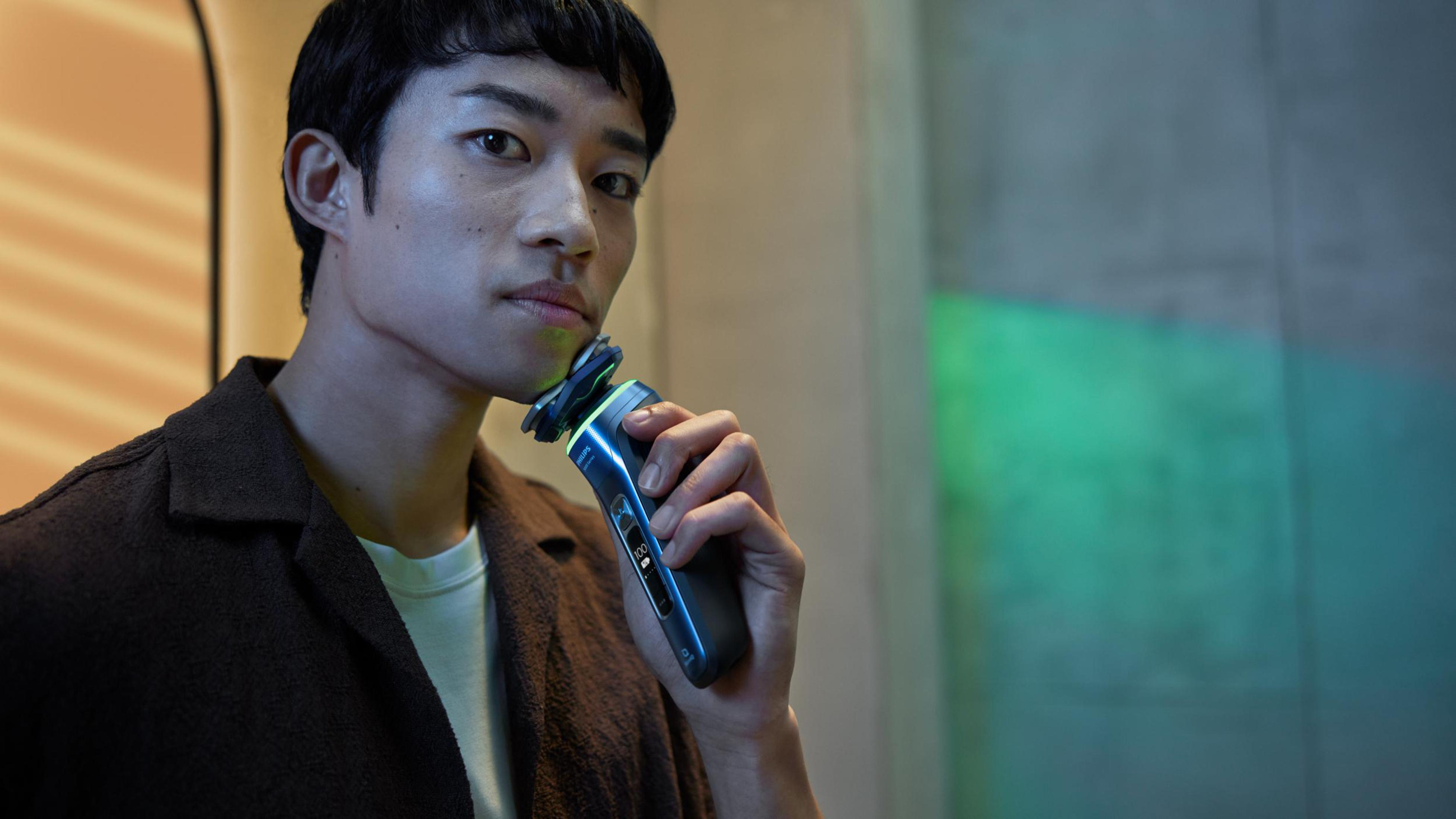 Mann rasiert sich mit Elektrorasierer, beleuchtet mit blauem und grünem Licht.