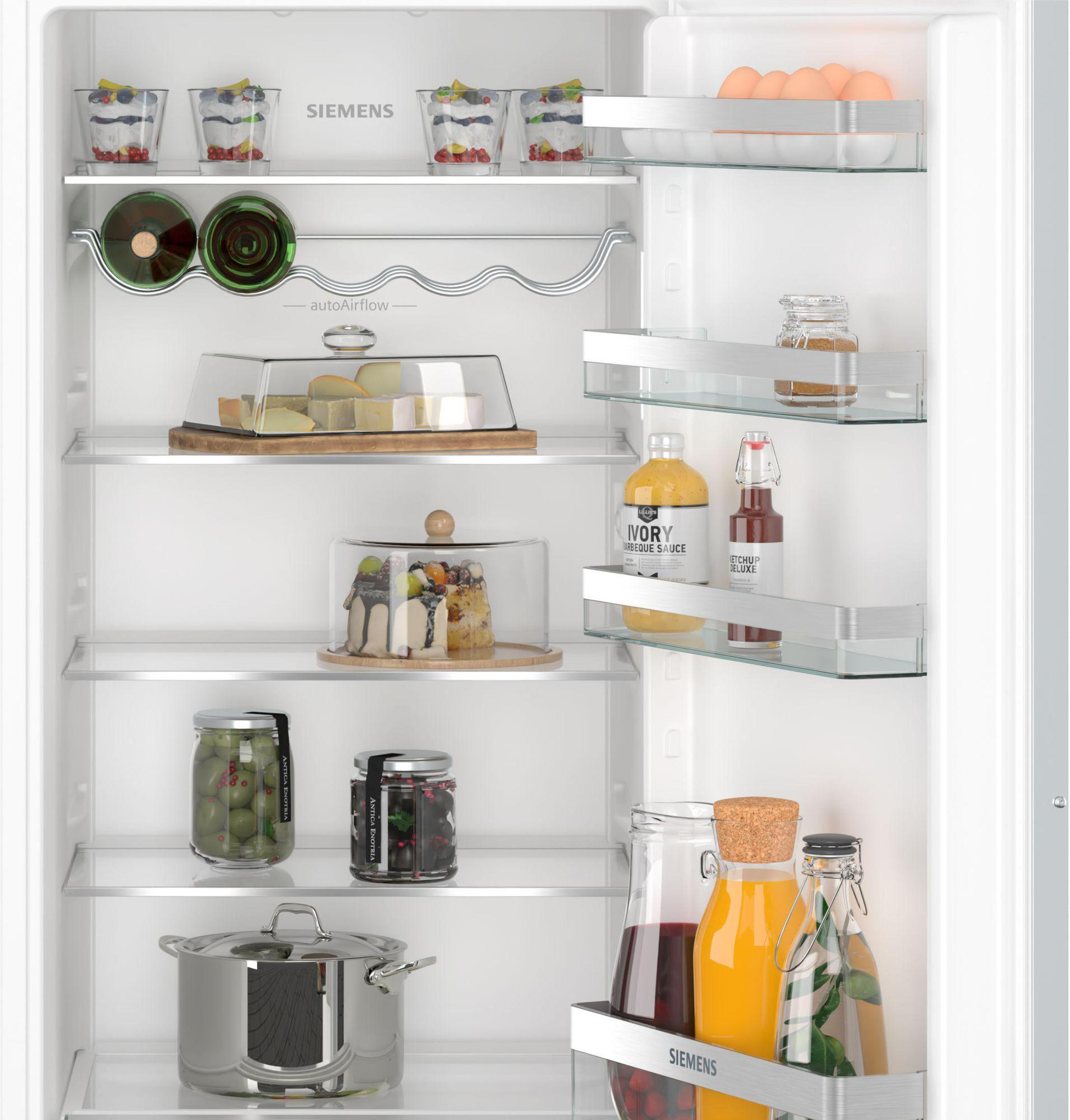 Kühlschrank mit Regalen voller Lebensmittel. Gläser, Flaschen und eine Auflaufform innen.