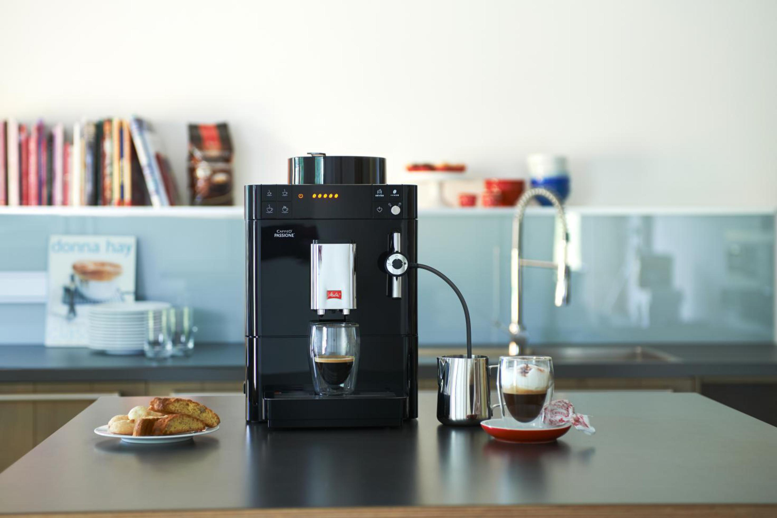 Máquina de espresso negra vertiendo café. Cocina en el fondo.