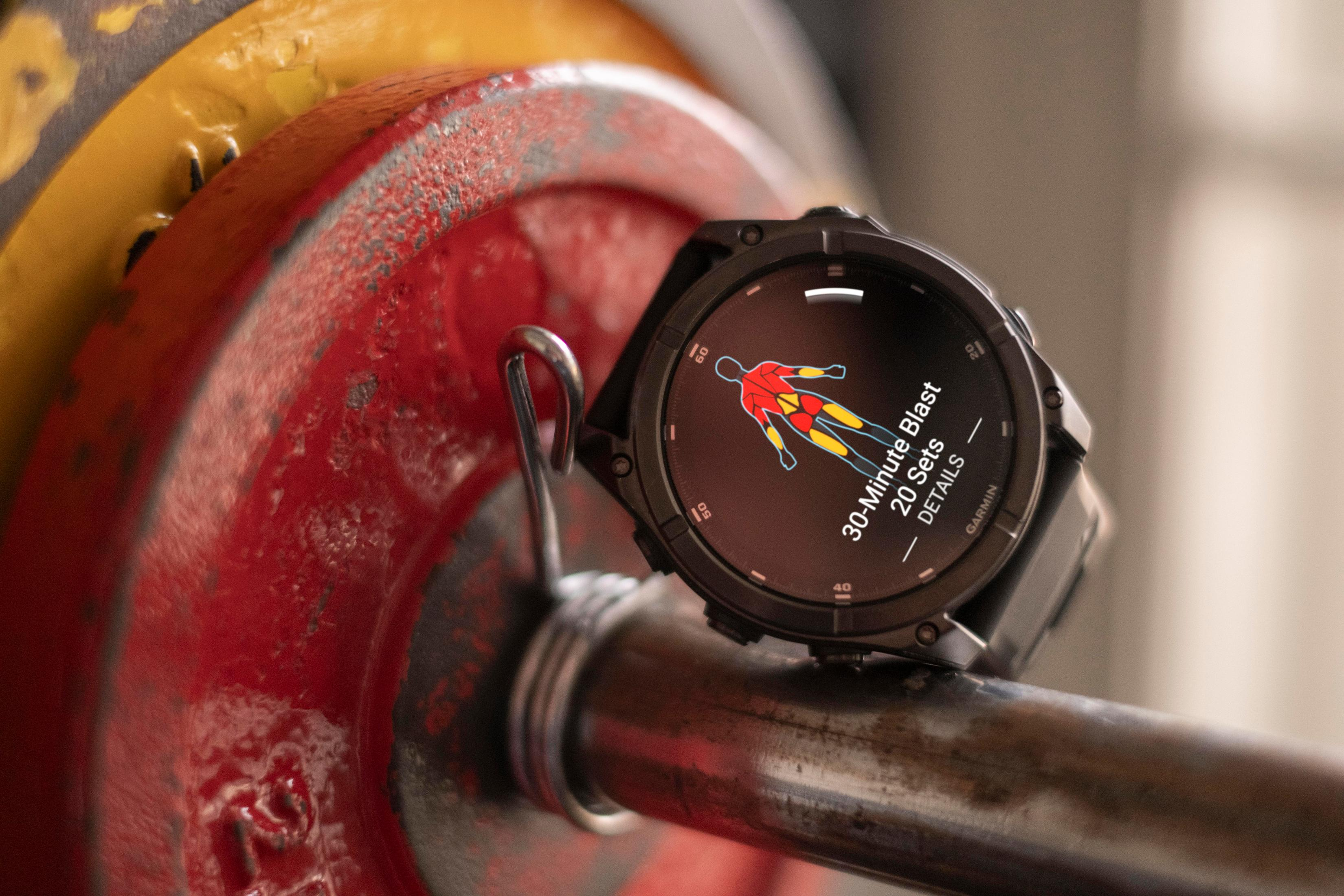 Smartwatch en una barra de pesas. El reloj muestra detalles del ejercicio. Pesa roja en el fondo.