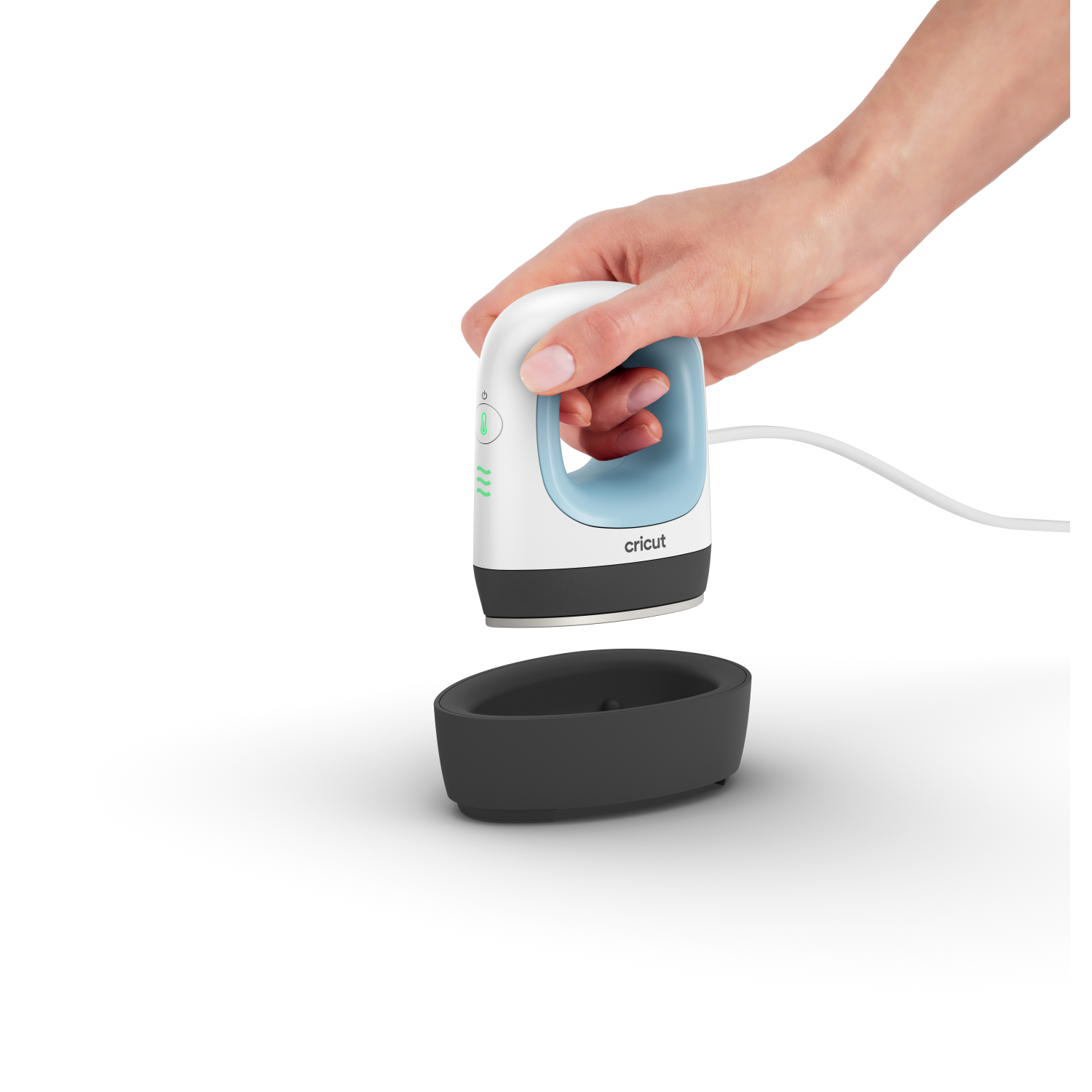 Mano sosteniendo una plancha Cricut mini blanca y azul, con base negra sobre fondo negro.