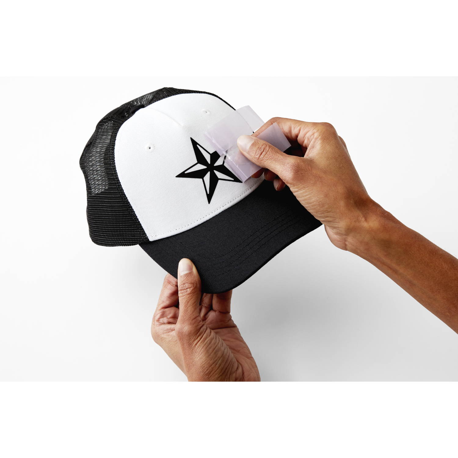 Mani che tengono un cappello bianco e nero con una stella, applicando un adesivo quadrato.