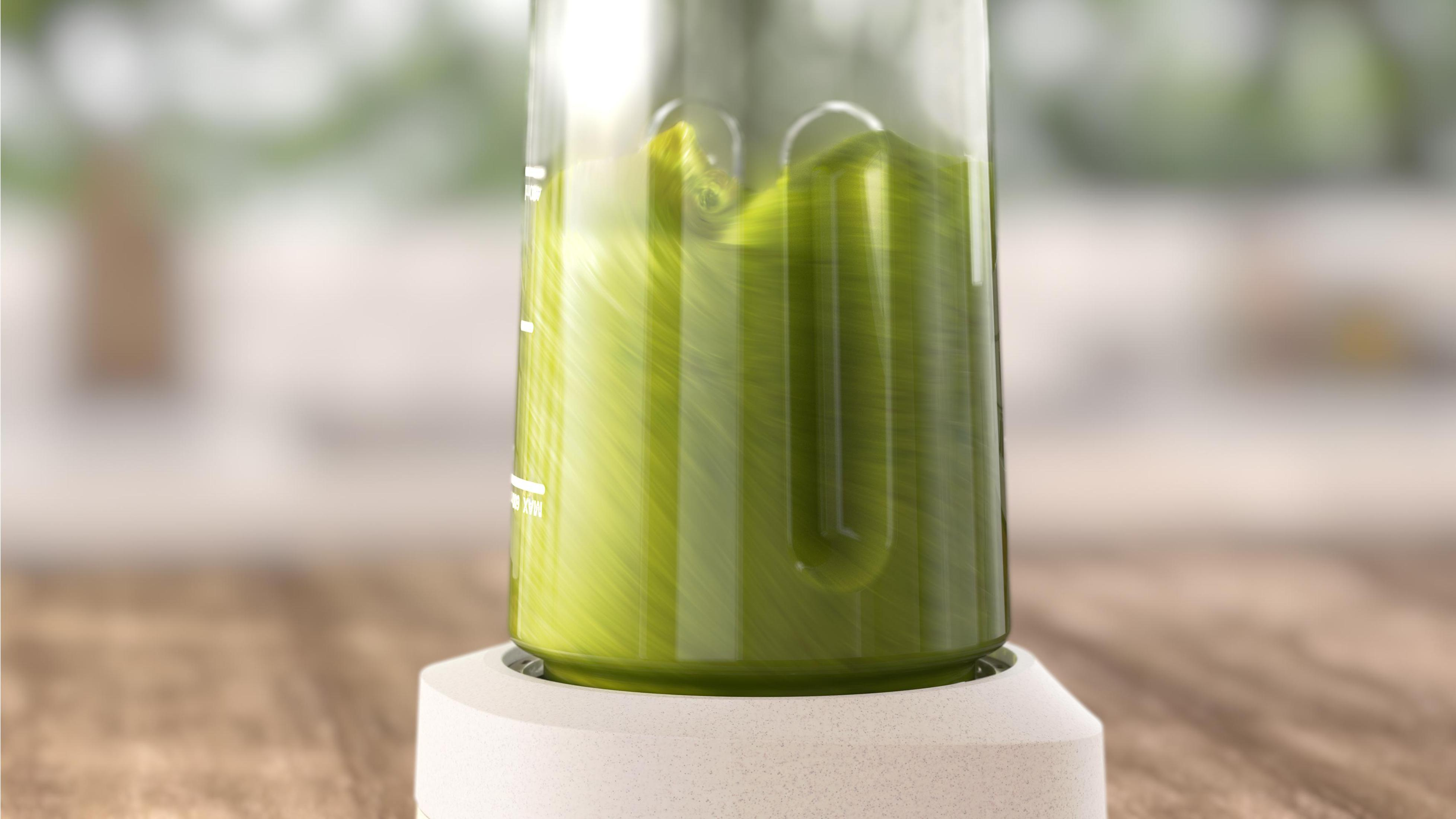 Ein Mixer in Aktion, gefüllt mit grüner Flüssigkeit. Wirbelnde Bewegung im Glas sichtbar.