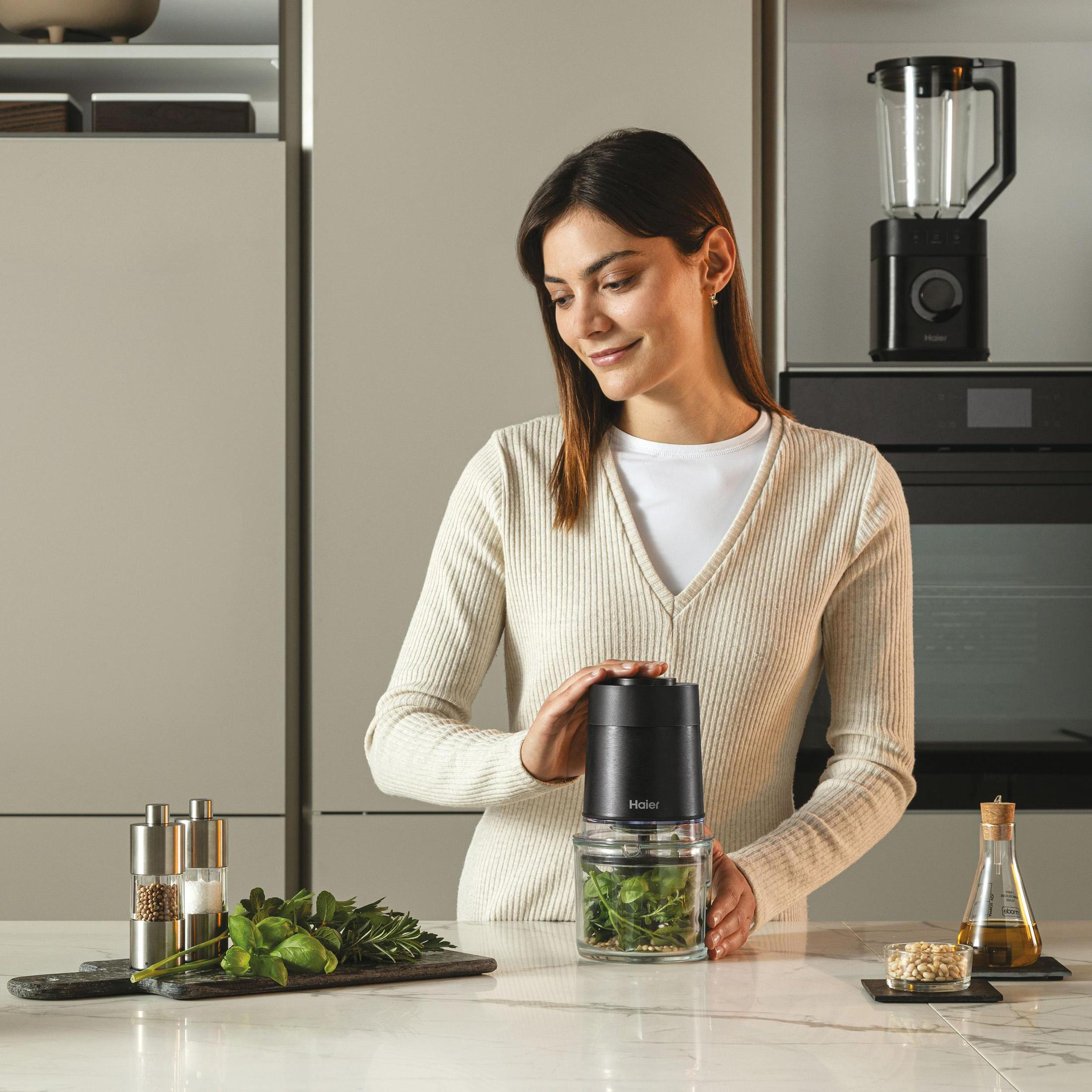 Donna usa un robot da cucina Haier, scena cucina con ingredienti nelle vicinanze.