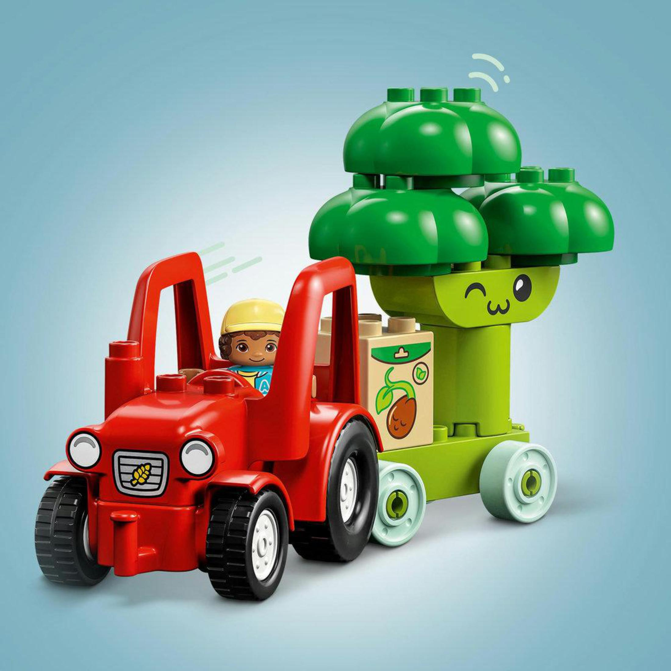 Un trattore Lego Duplo rosso traina un rimorchio verde a forma di albero, con un personaggio alla guida.