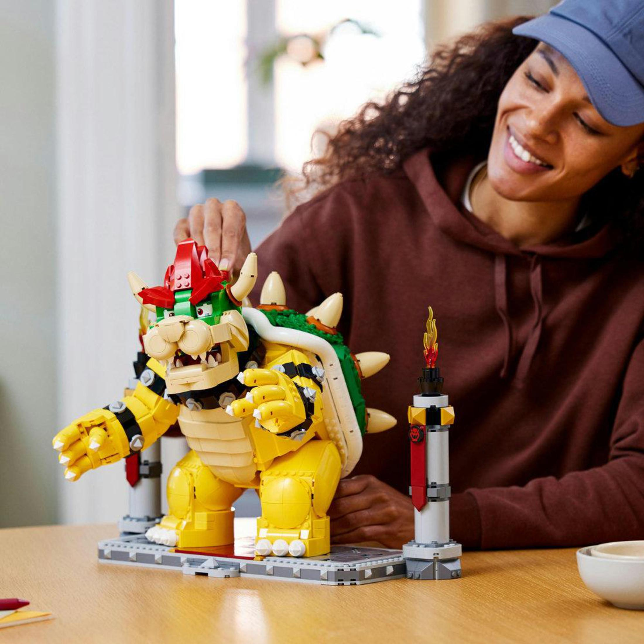 Kobieta montująca dużą figurę Lego Bowser. Kolory żółty, zielony i czerwony.