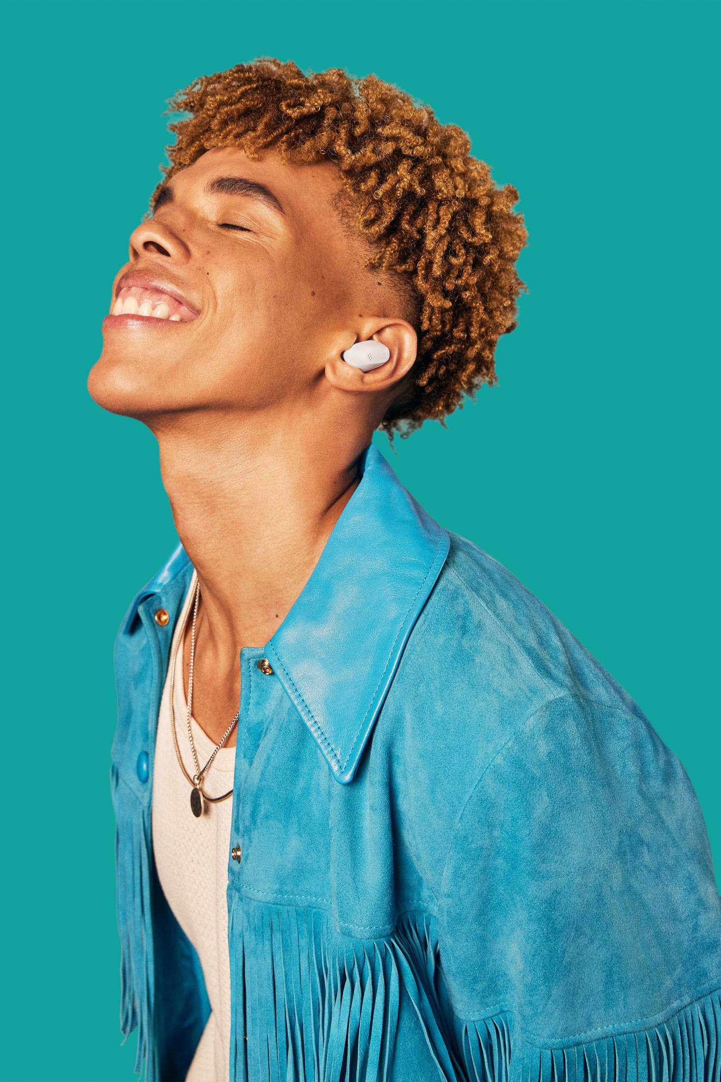 Persona sonriendo con auriculares, chaqueta azul y collar, fondo turquesa.