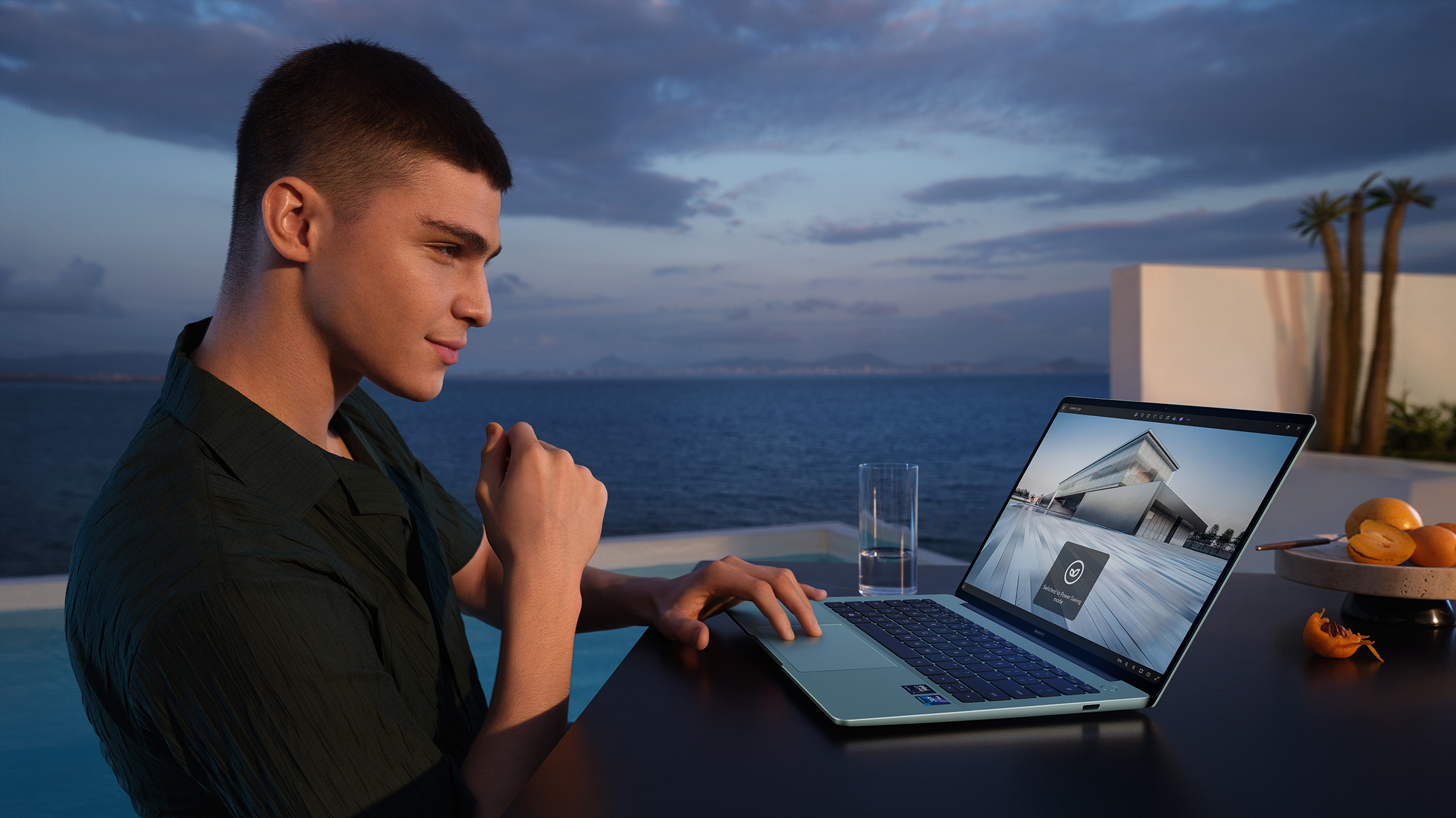 Mann, der im Freien einen Laptop benutzt. Hintergrund zeigt Wasser, Himmel und ein Glas Wasser. Laptop ist offen.