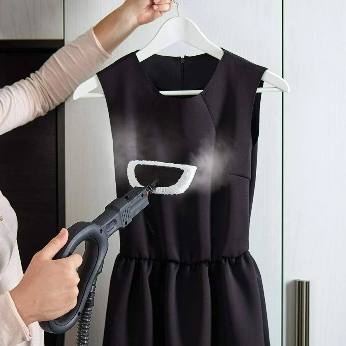 Una persona che stira un vestito nero su un'appendiabiti con un vaporizzatore portatile.