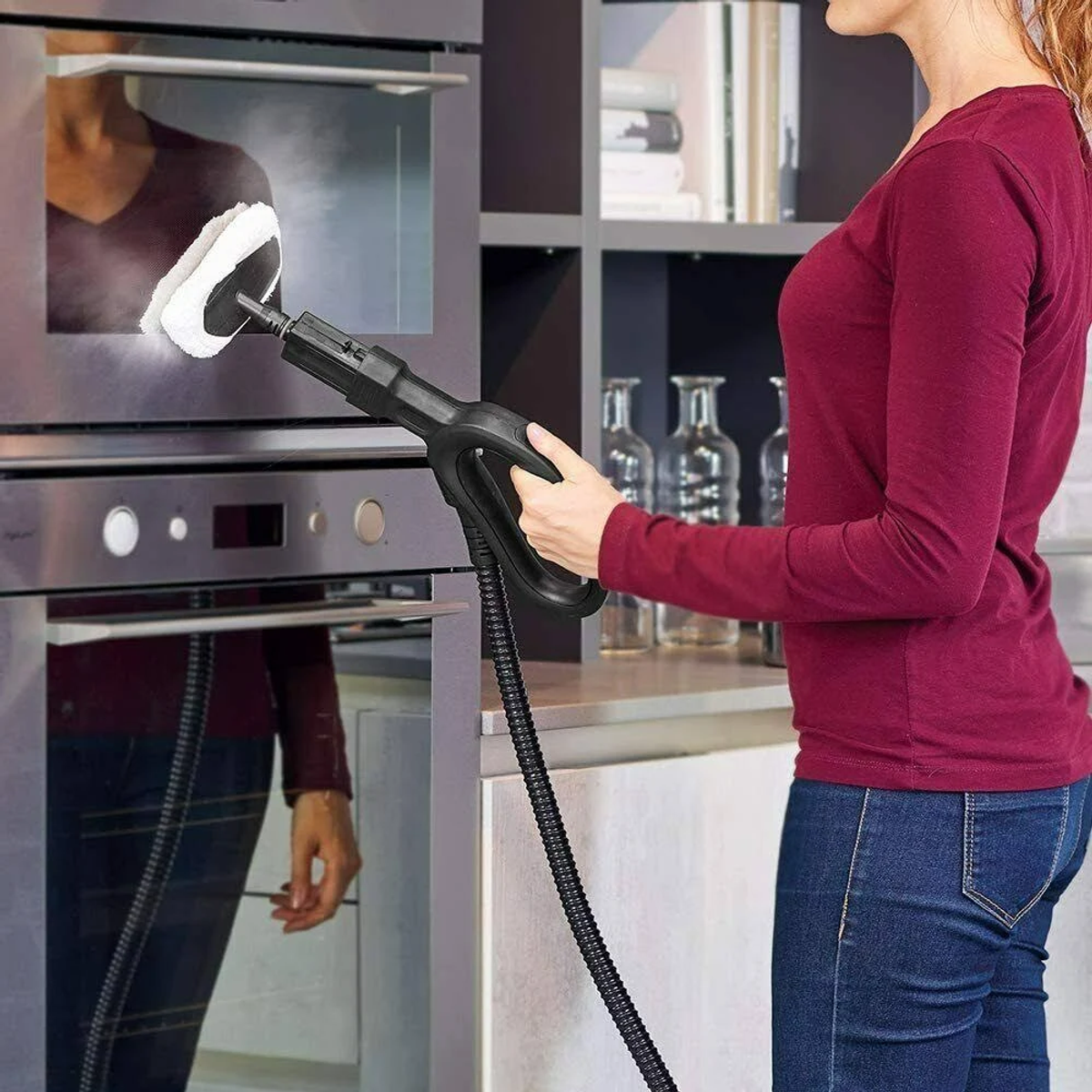 Donna che pulisce forno con pulitore a vapore, riflesso nella porta.