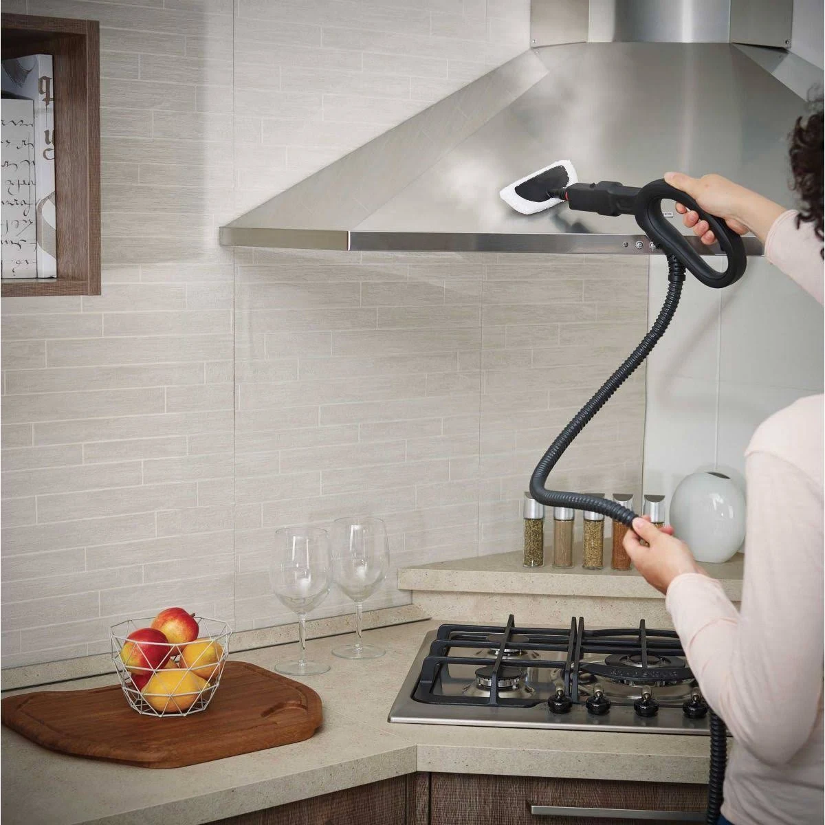 Osoba czyści okap ze stali nierdzewnej za pomocą parownicy. Ustawienie kuchni z owocami.