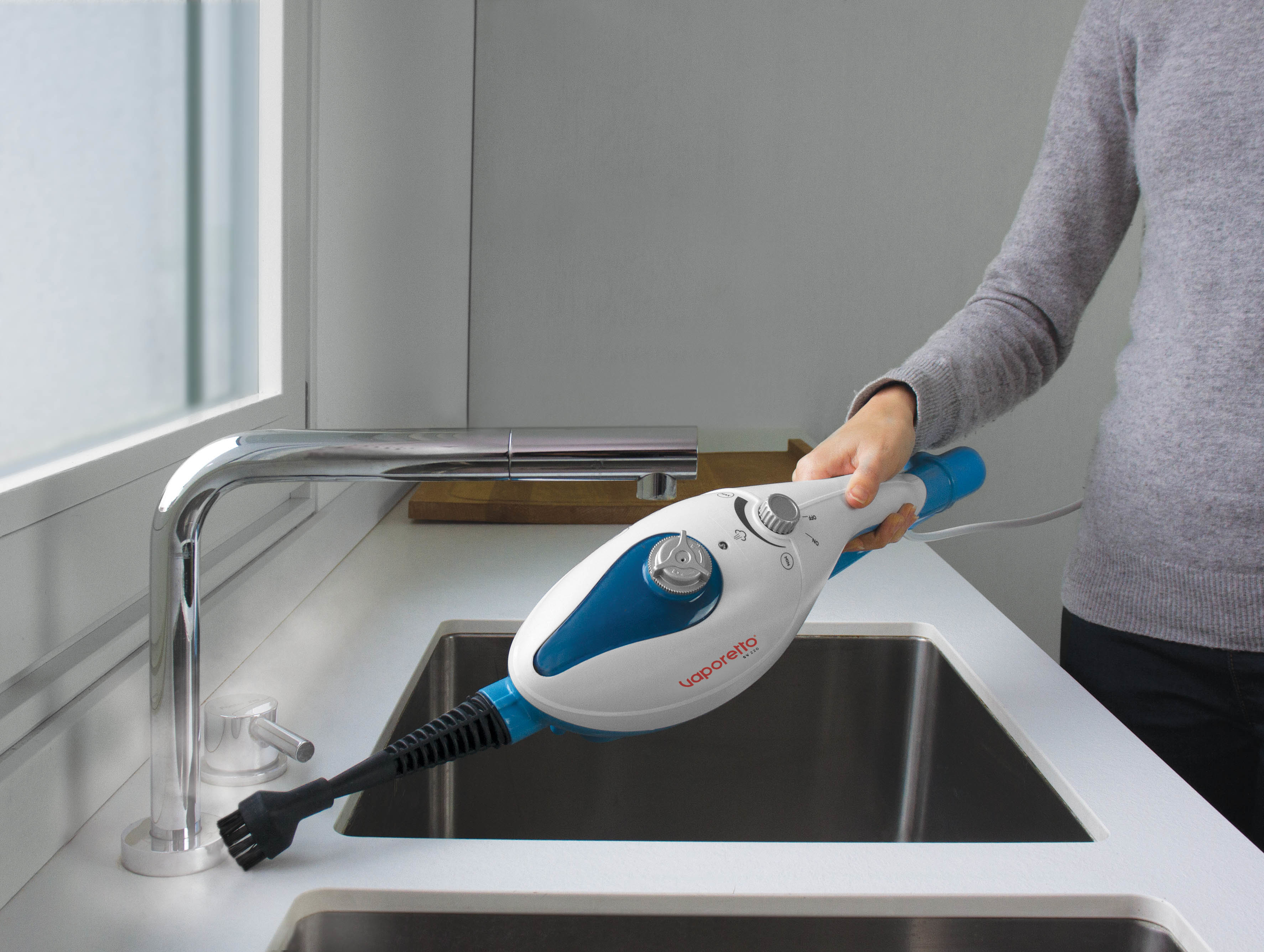 Kobieta czyści zlew niebiesko-białym parownikiem. Widoczna srebrna bateria.