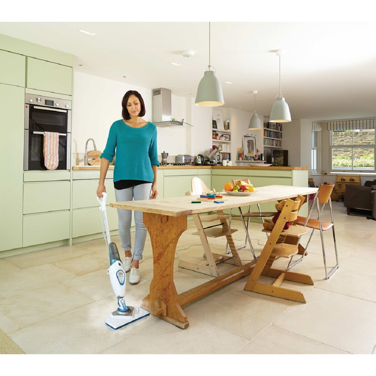 Kobieta używa mopa parowego na kafelkach w kuchni. Drewniany stół i krzesła.