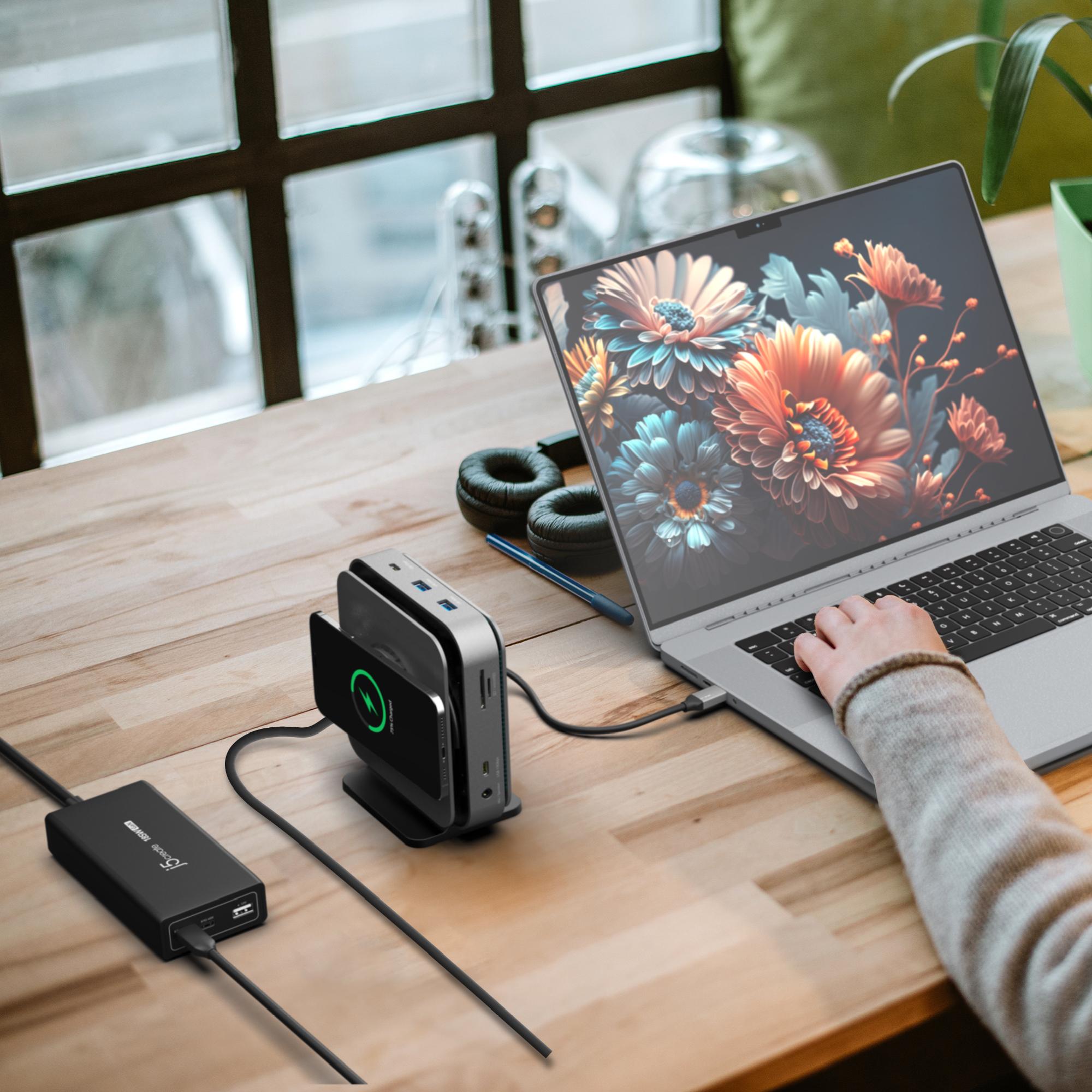 Un ordinateur portable sur une table en bois avec station de charge et casque. Une personne tape.