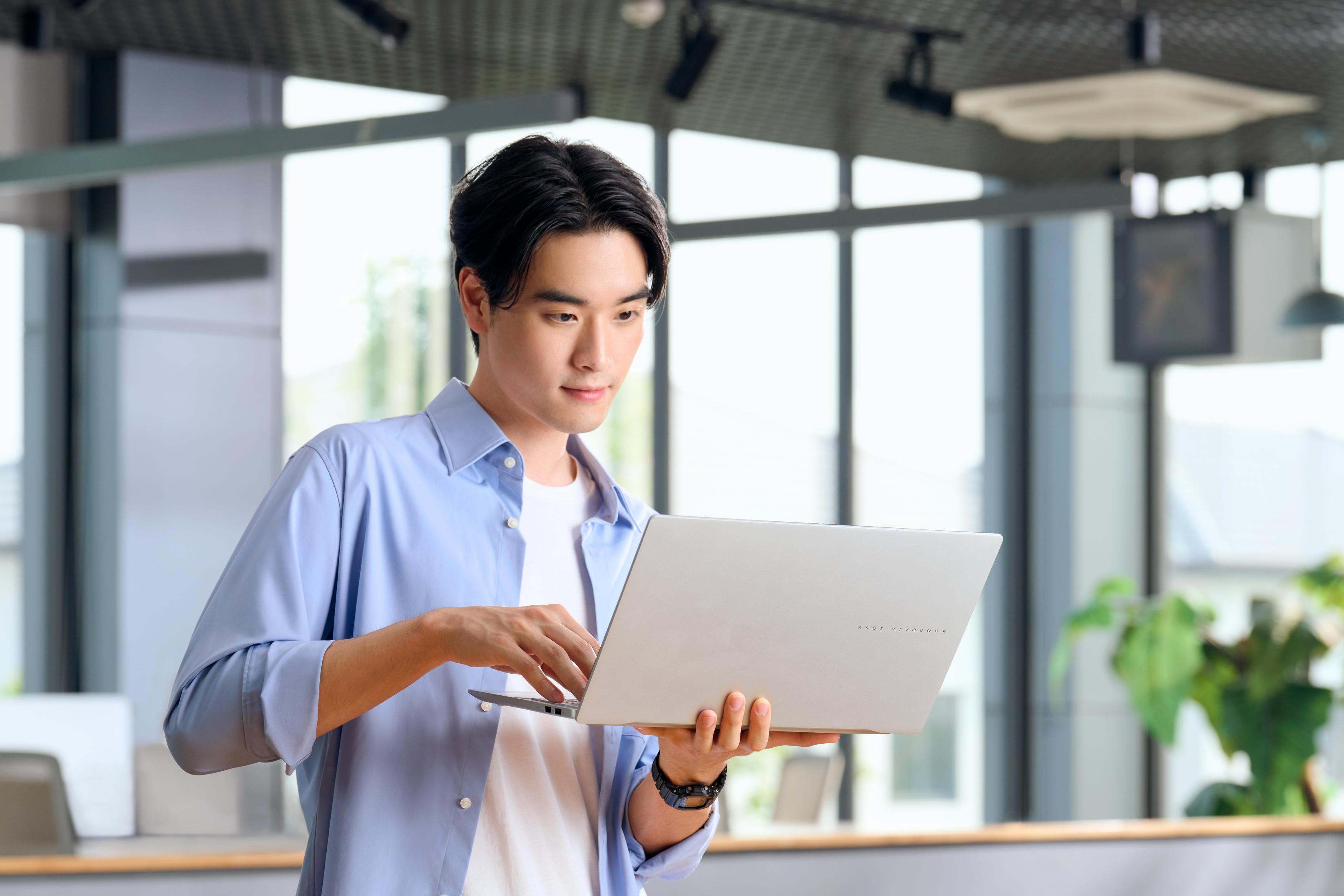 Asiatischer Mann arbeitet in einer hell beleuchteten Büroumgebung an einem Laptop.