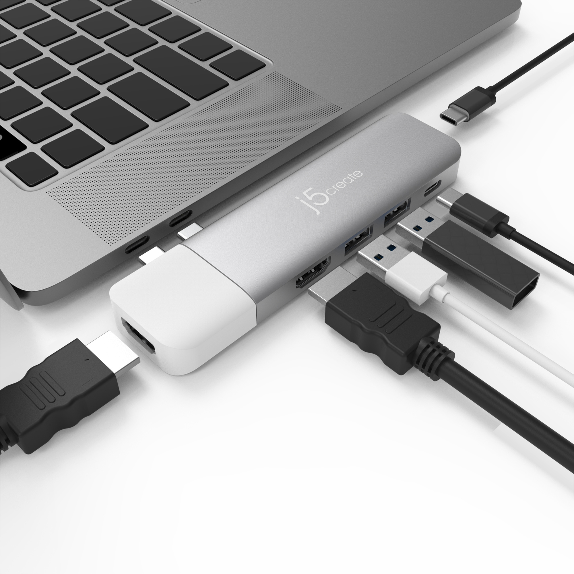 Laptop mit silbernem Hub und angeschlossenen Kabeln. USB, HDMI und andere Anschlüsse sichtbar.