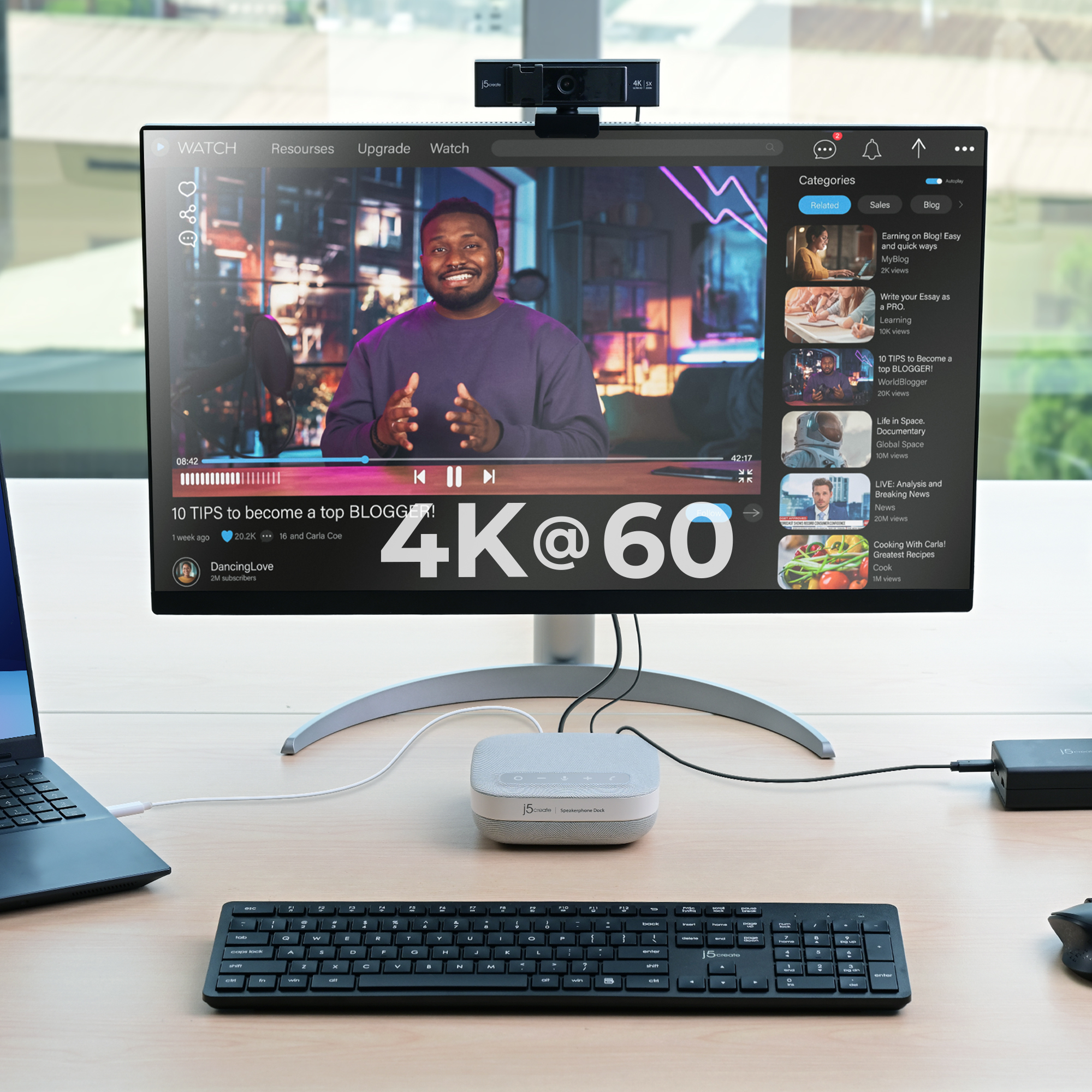 Ein Schreibtisch-Setup mit Monitor, Webcam, Tastatur, Lautsprechern und Laptop.