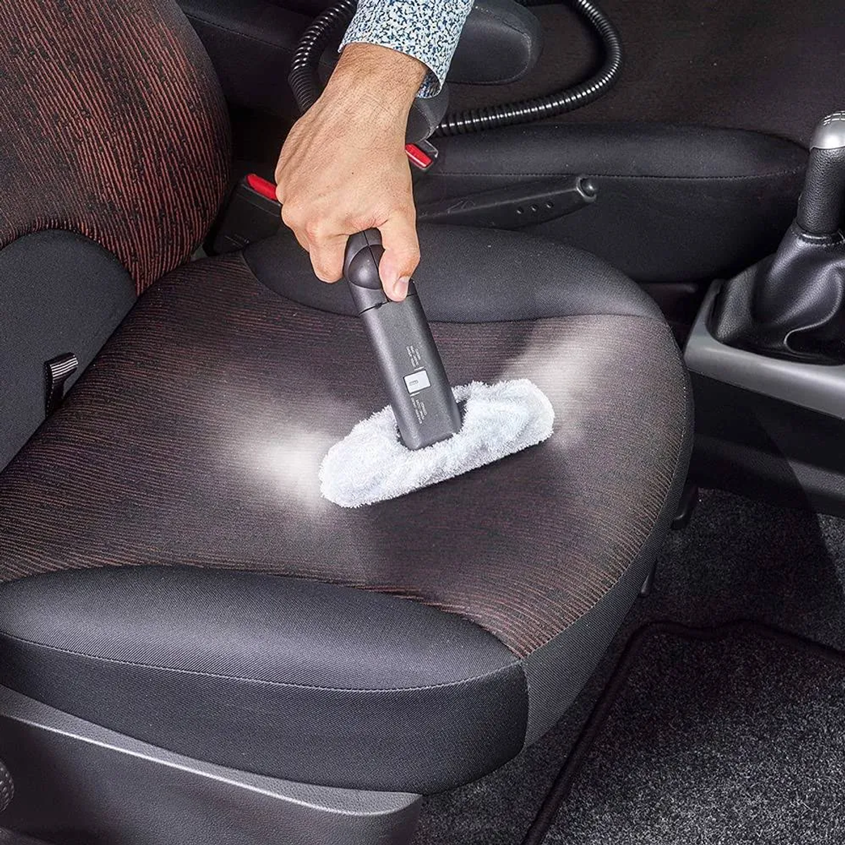 Persona che pulisce un sedile auto con un pulitore a vapore portatile. Attacco in tessuto bianco.