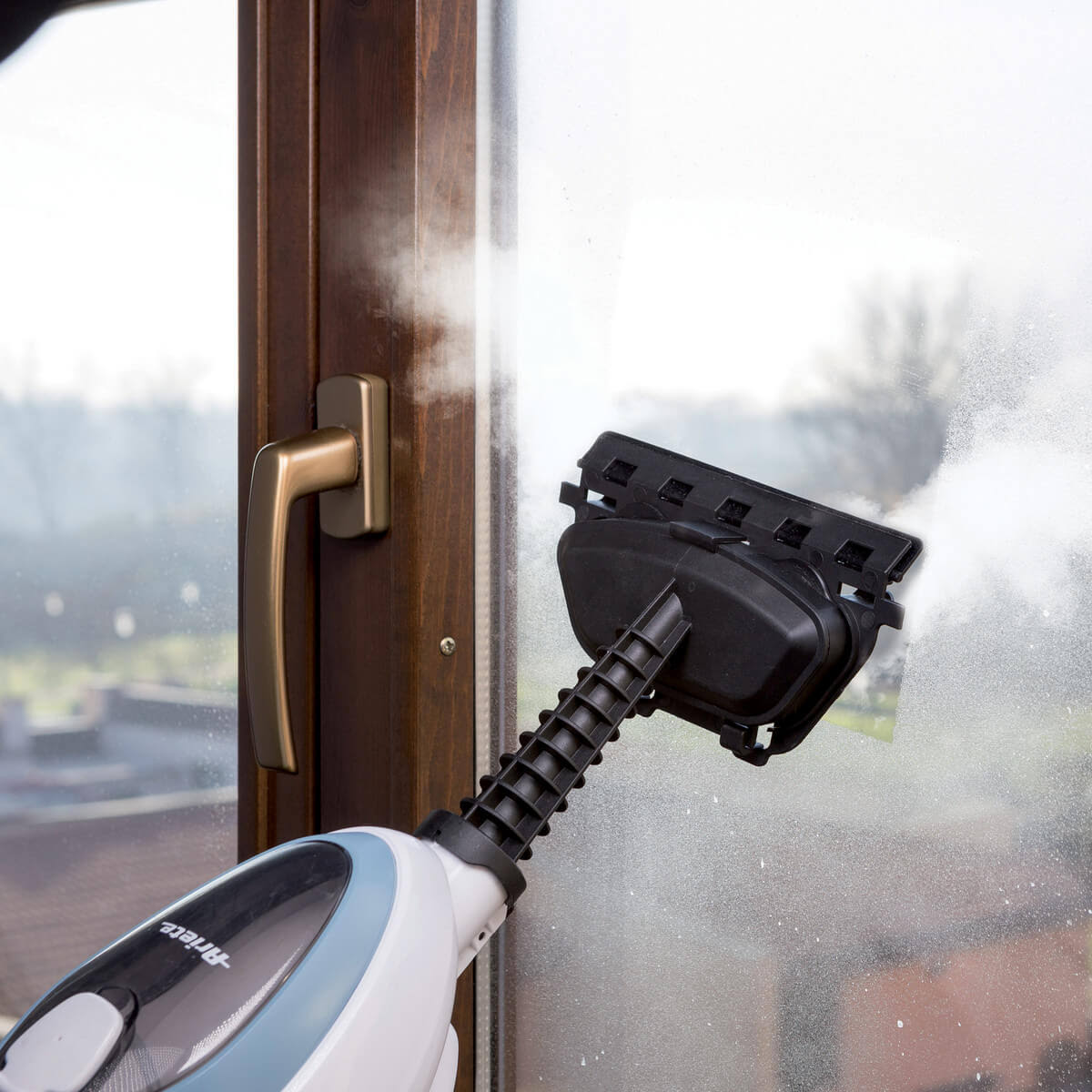 Oczyszczacz parowy na oknie. Czarna głowica, uchwyt i biały korpus. Brązowa rama okienna.