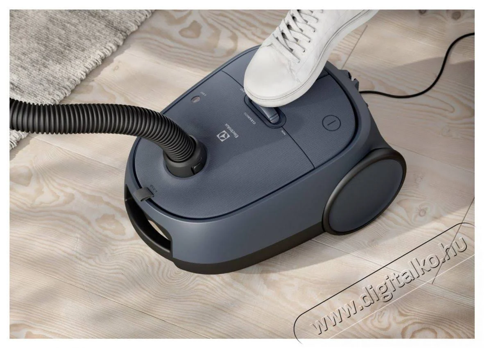 A person's foot stepping on a blue vacuum cleaner, with an angled hose.