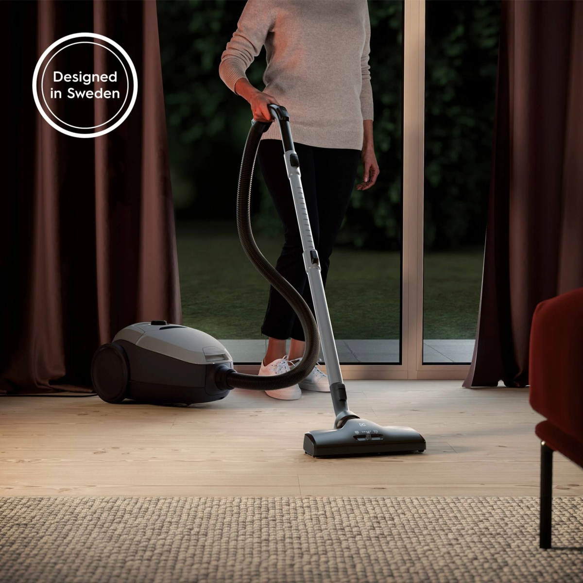 Kobieta używająca odkurzacza na drewnianej podłodze, z szarym odkurzaczem, w pokoju.