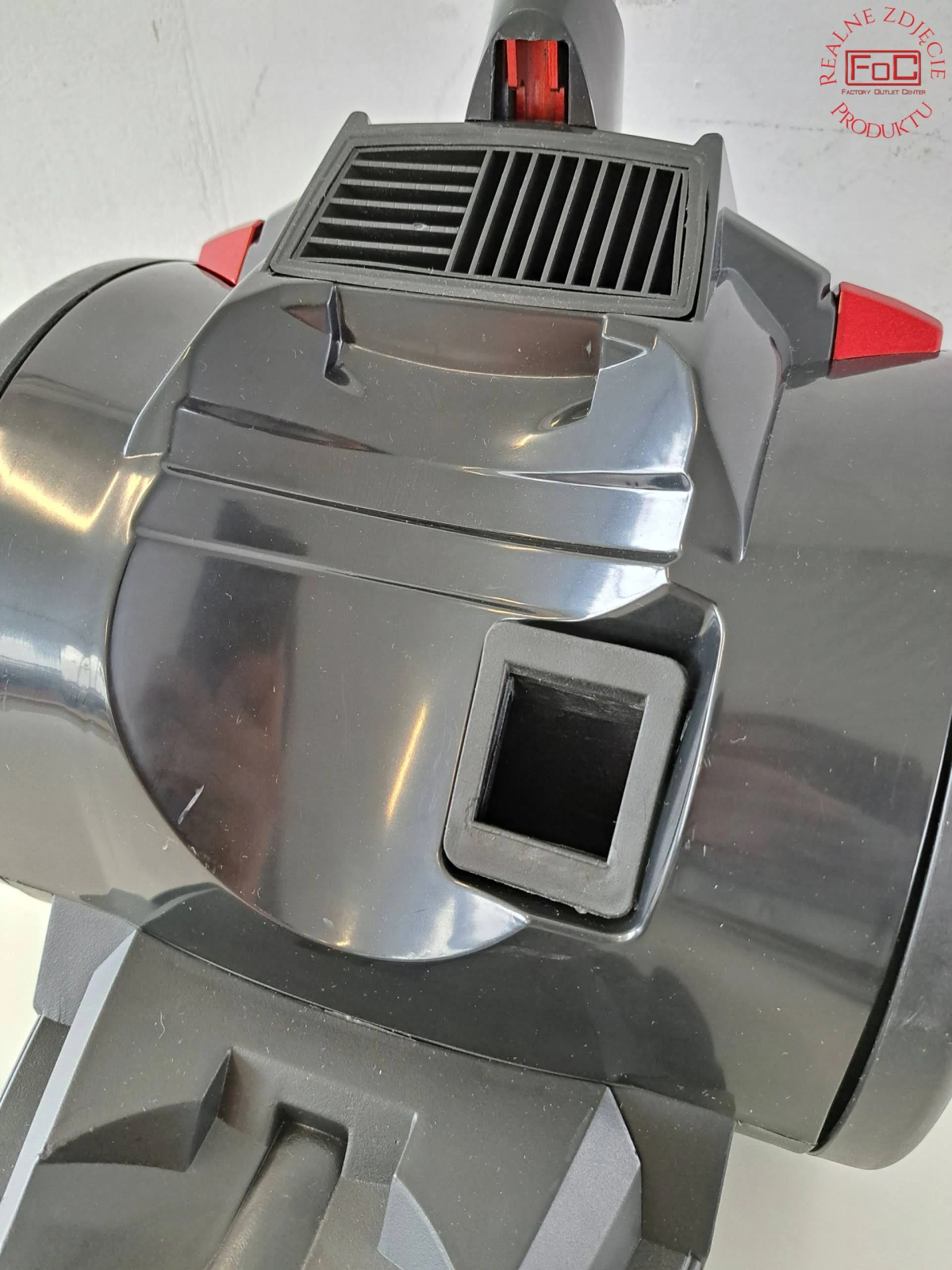 Zbliżenie na górną część czarnego odkurzacza. Czerwone akcenty i kwadratowy otwór.
