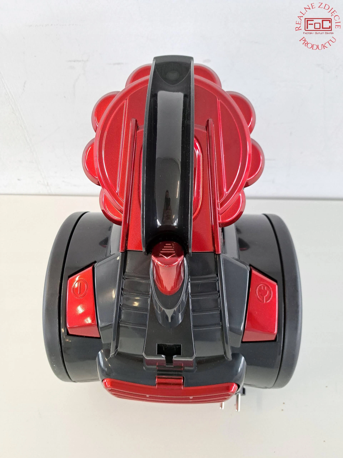 Czerwony i czarny odkurzacz, widziany z góry, na białej powierzchni.
