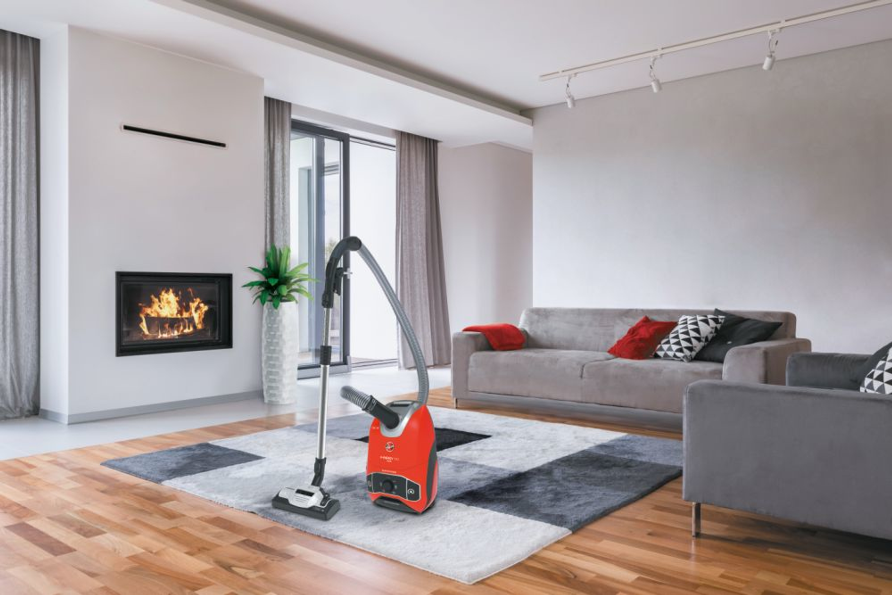 Salon z odkurzaczem na wzorzystym dywanie, kominkiem i sofą.