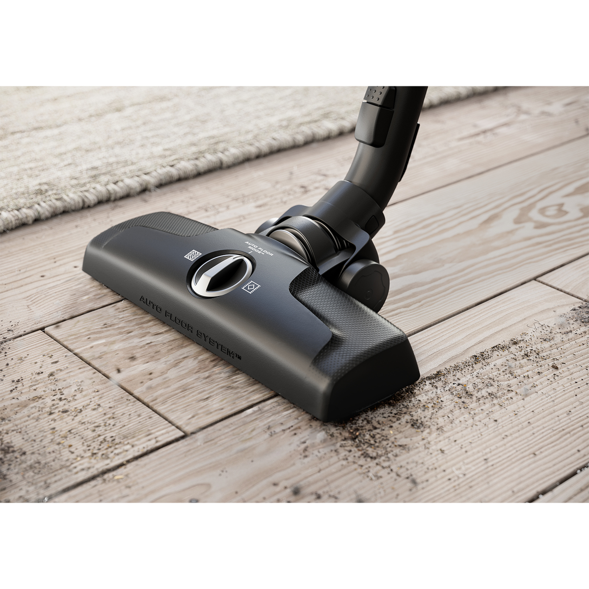 Czarna głowica odkurzacza na drewnianej podłodze, sprząta kurz. Jasny dywan w tle.