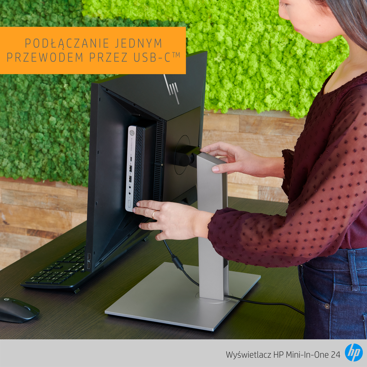 Vrouw met een monitor. Monitor heeft witte bevestiging. Bureau met muis. Groene muur.