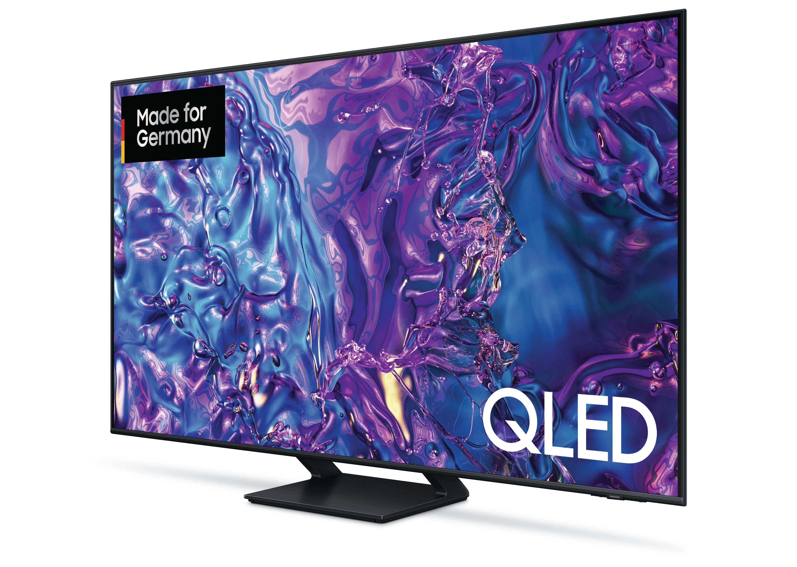 Duży telewizor Samsung QLED. Czarna ramka, podstawa. Fioletowy i niebieski abstrakcyjny obraz na ekranie. Białe tło.