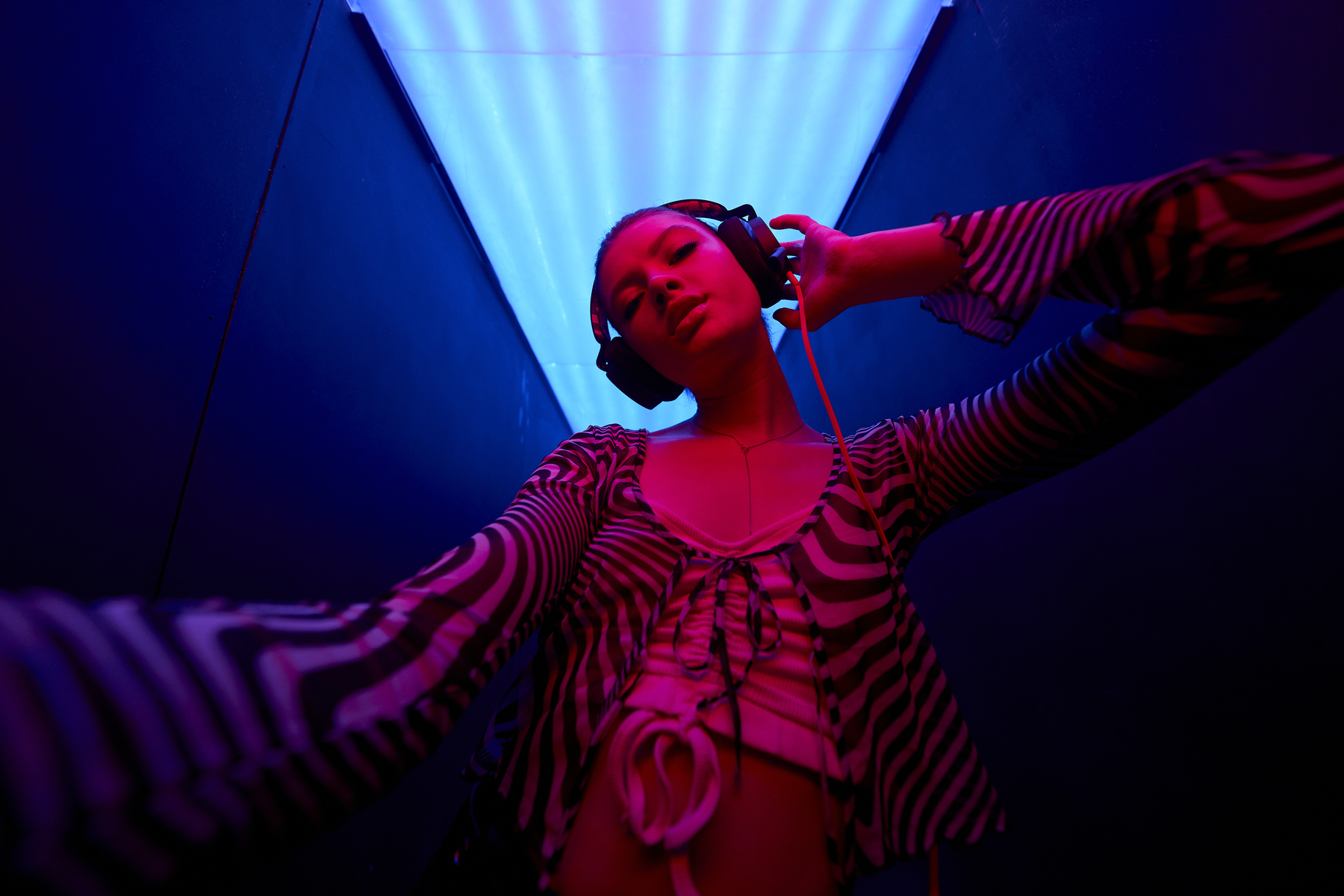Donna in un club, con le cuffie e una camicia fantasia. La scena è illuminata con luci rosse e blu.