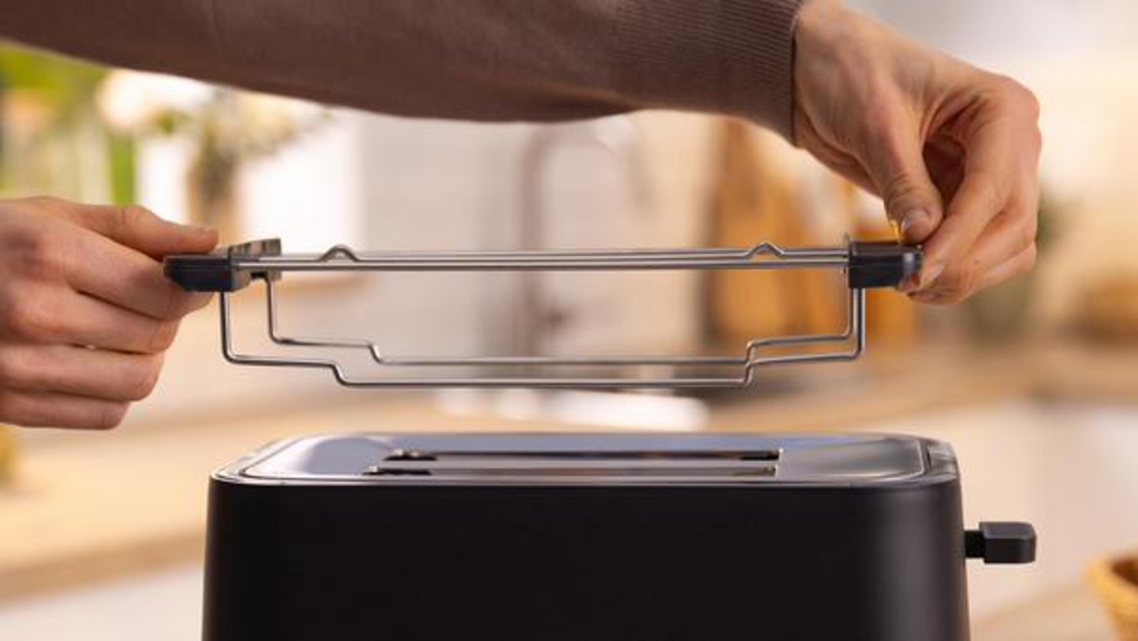 Ręce trzymające ruszt do tostera nad czarnym tosterem.