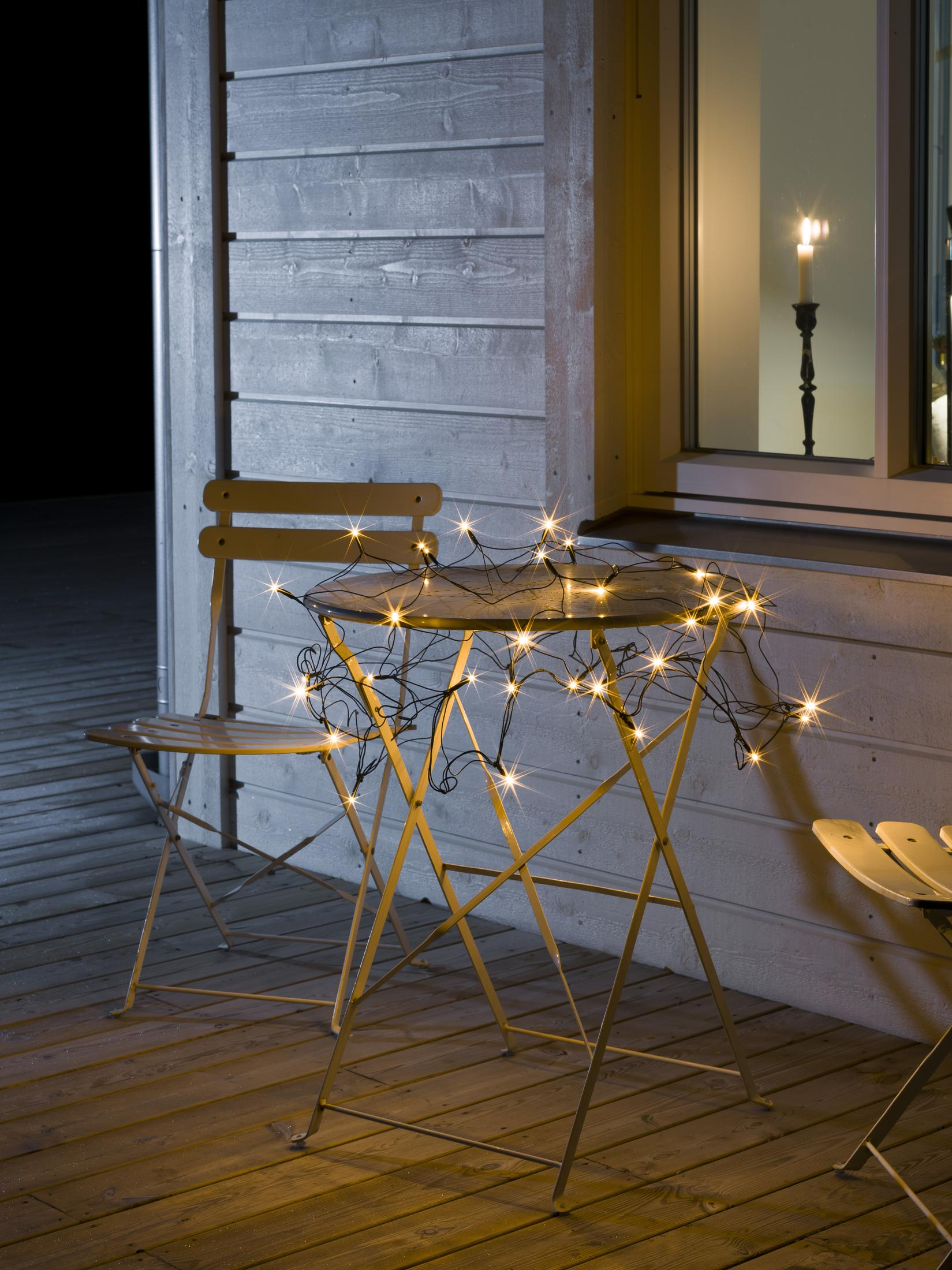 Tisch mit Lichterketten. Kerze im Fenster. Holzdeck und Wand.
