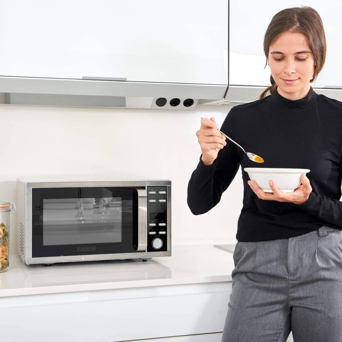 Donna in cucina con una ciotola di zuppa, microonde sullo sfondo.