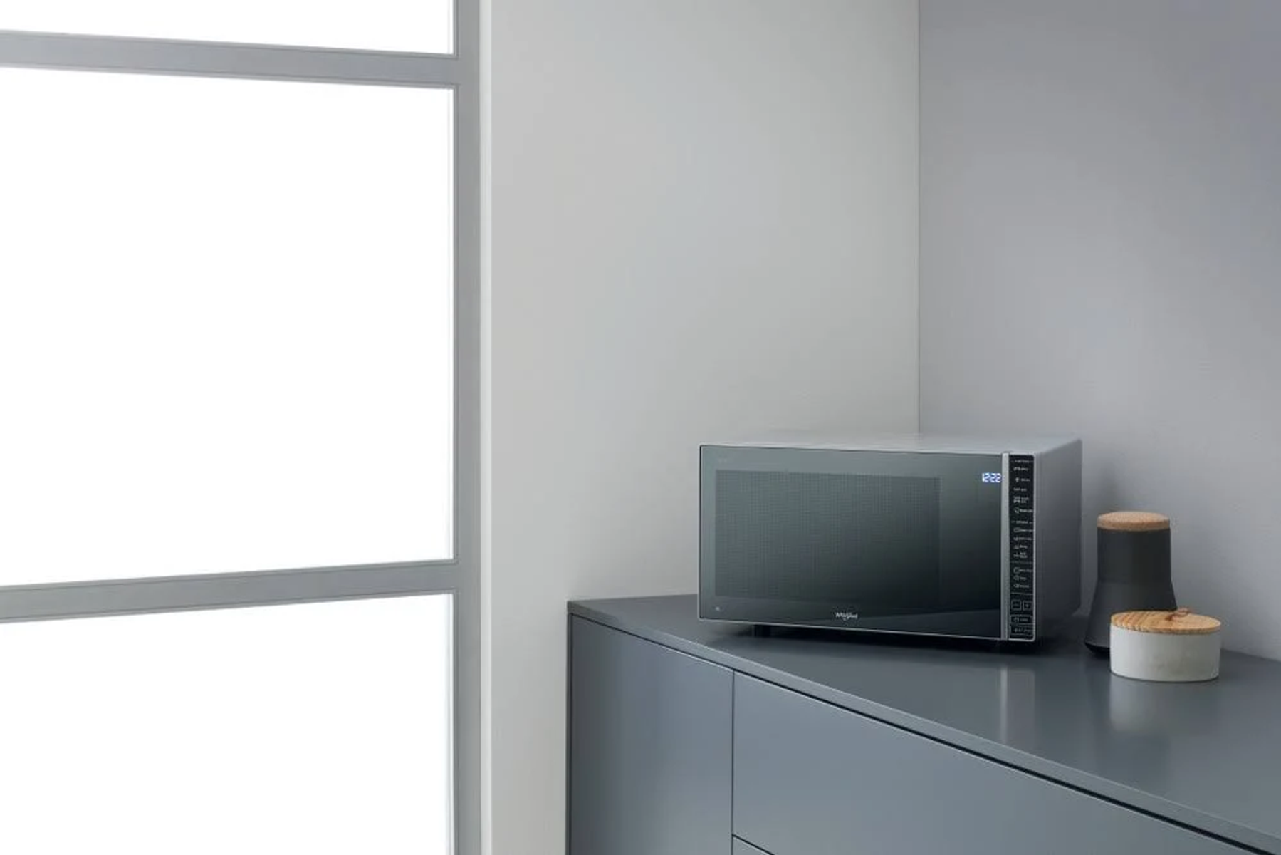 Kuchenka mikrofalowa na szarym blacie w kuchni. W pobliżu okno i elementy dekoracyjne.
