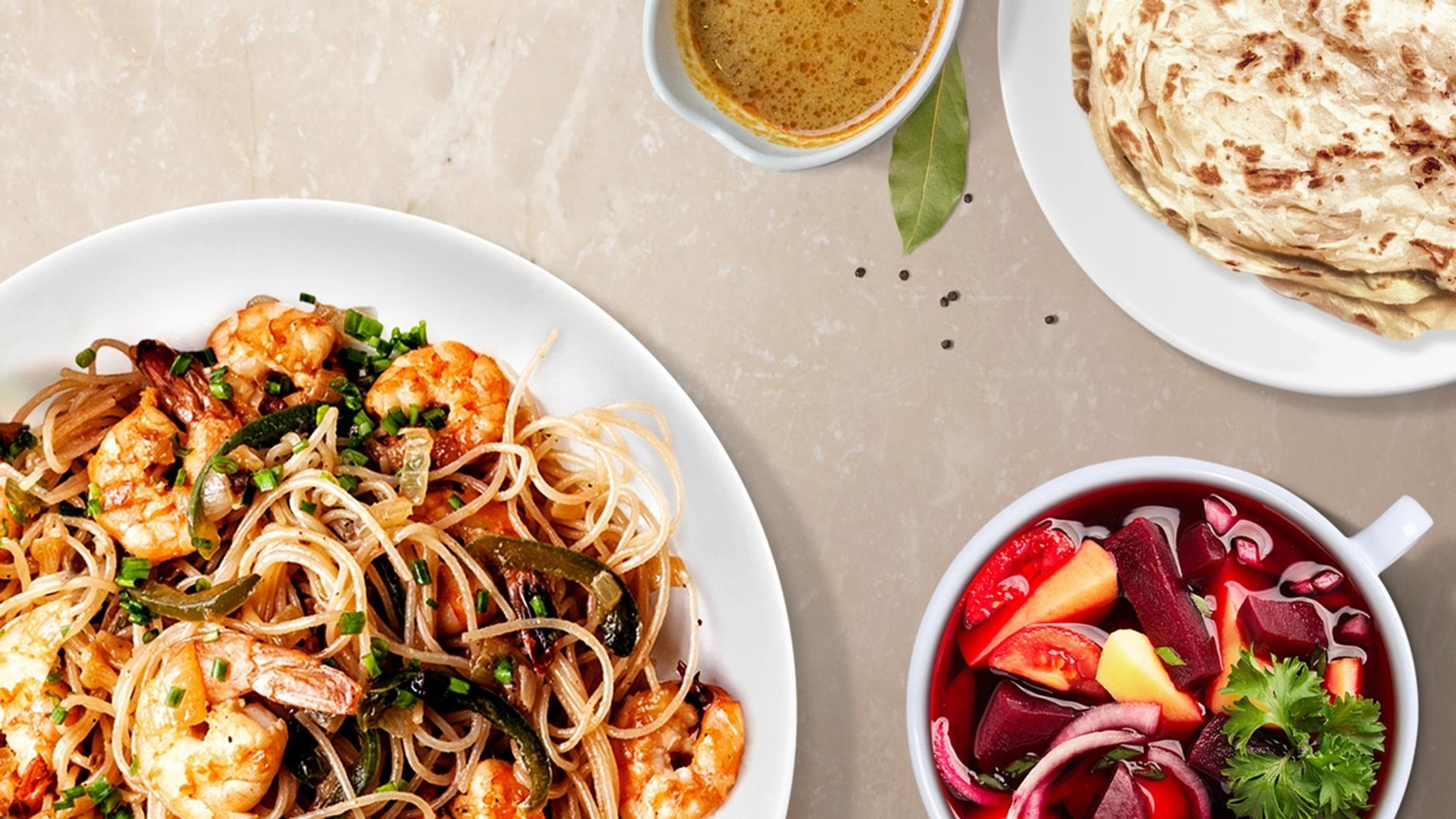 Un tavolo con vari piatti, tra cui noodles con gamberi, zuppa e pane.