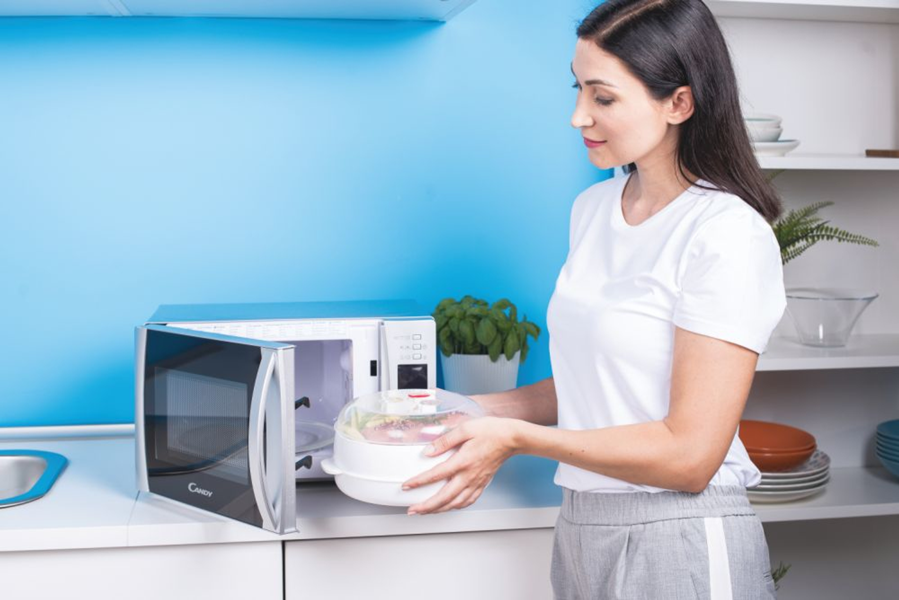 Una mujer coloca un recipiente con comida dentro de un horno microondas.