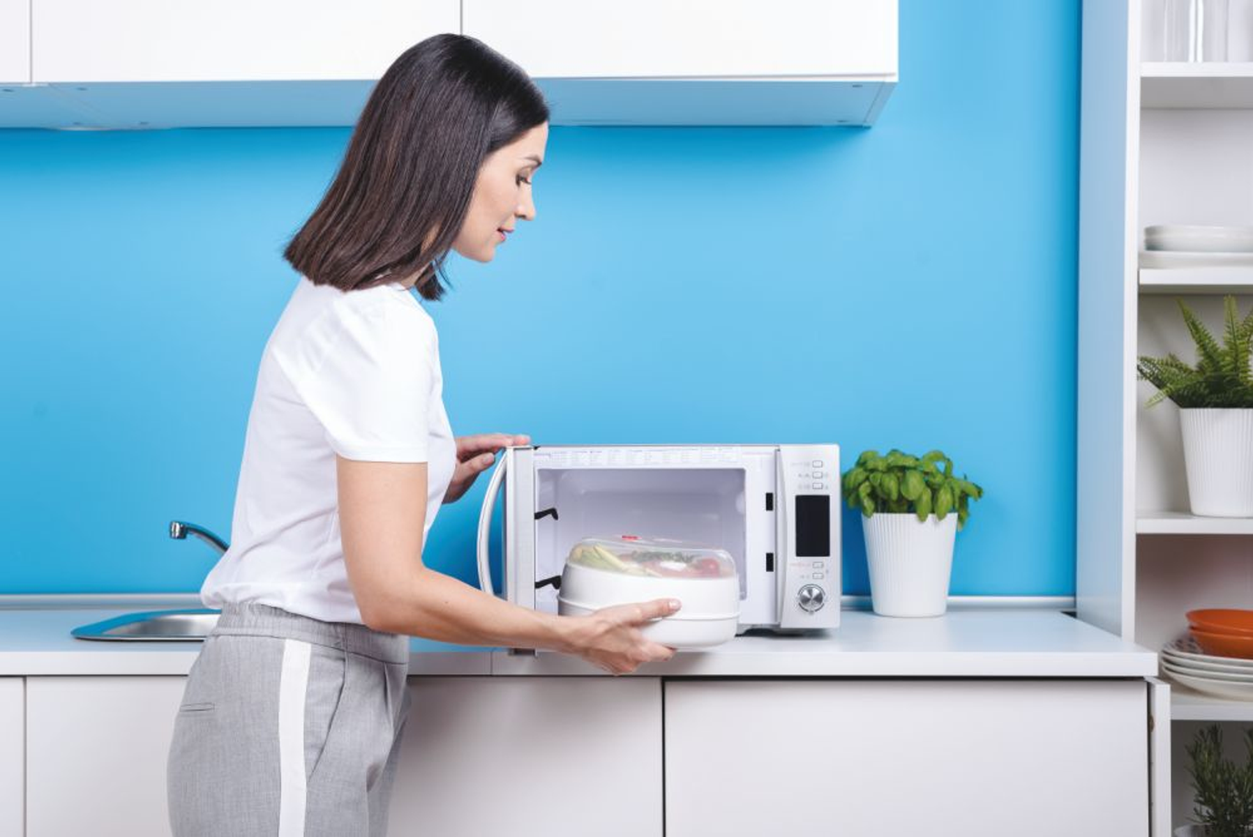 Mujer colocando un cuenco en un horno microondas blanco. Pared azul de fondo.