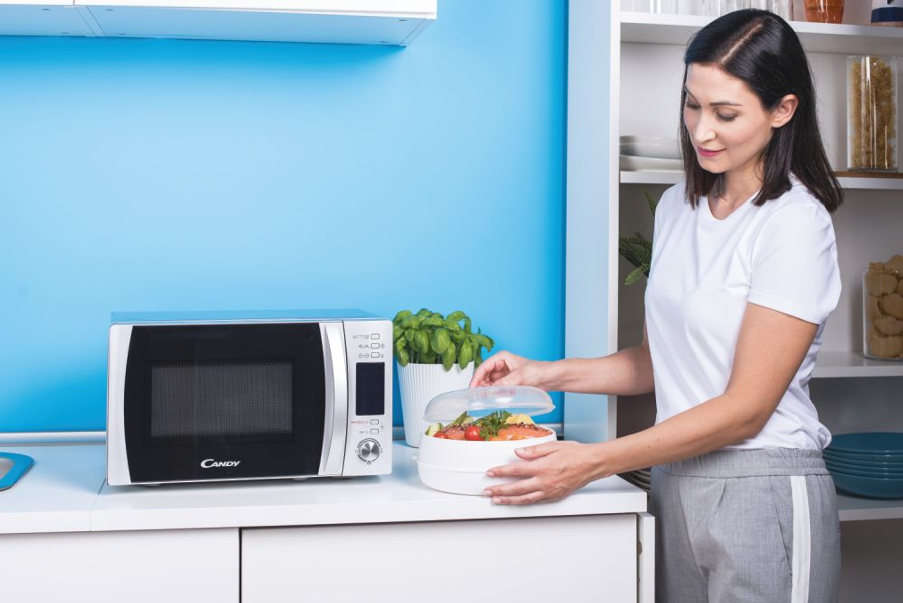 Mujer en una cocina con microondas poniendo una tapa en una vaporera de microondas.