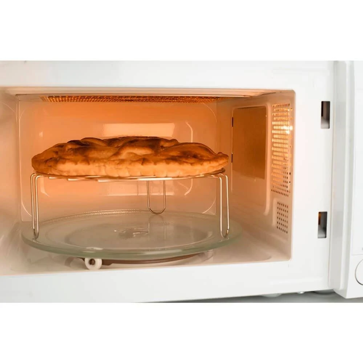 Kuchenka mikrofalowa z upieczonym ciastem w środku, na metalowym stojaku nad szklanym talerzem.