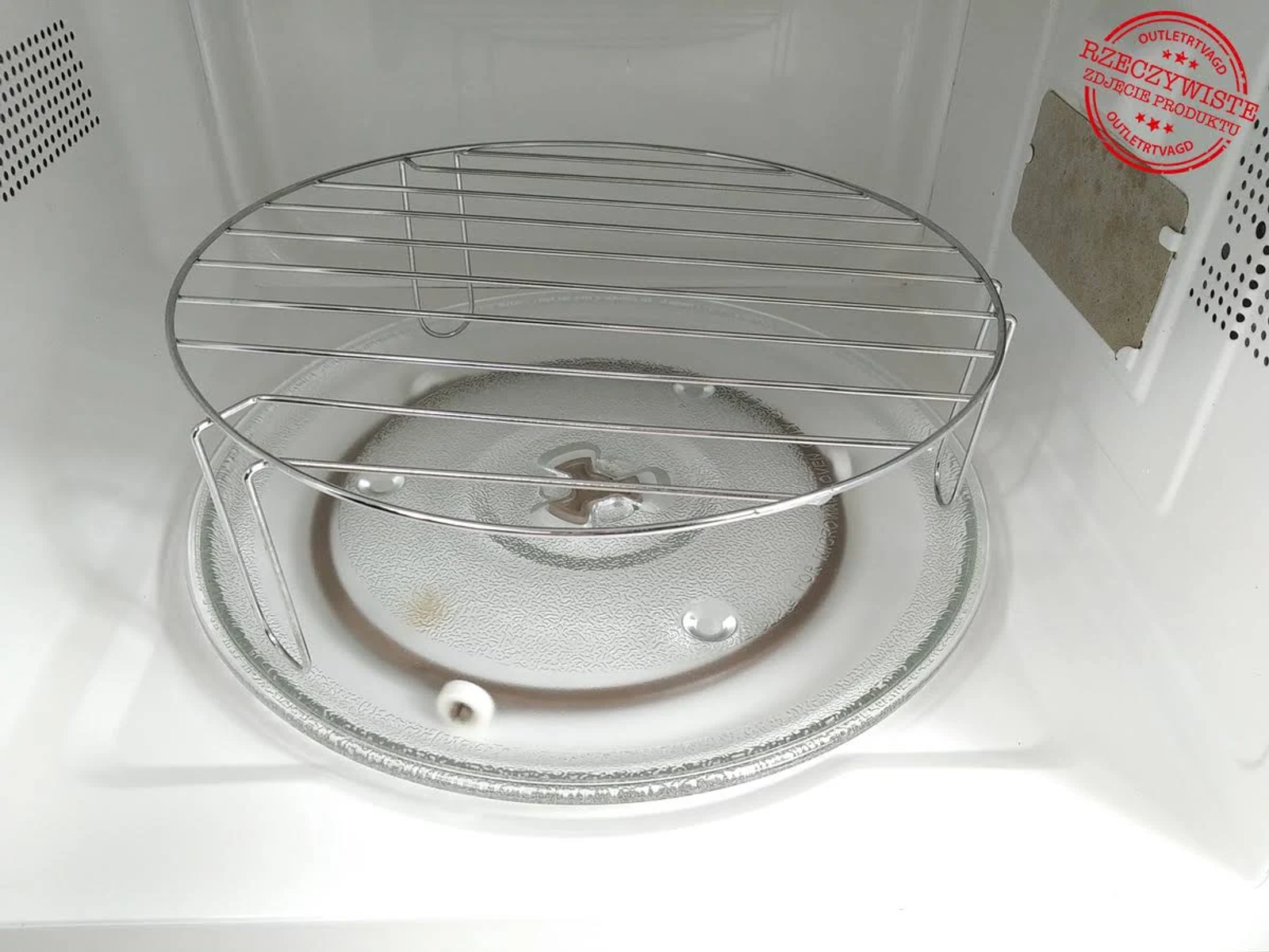 Wnętrze kuchenki mikrofalowej. Szklany talerz i metalowy stojak. Białe wnętrze. Naklejka z tekstem.