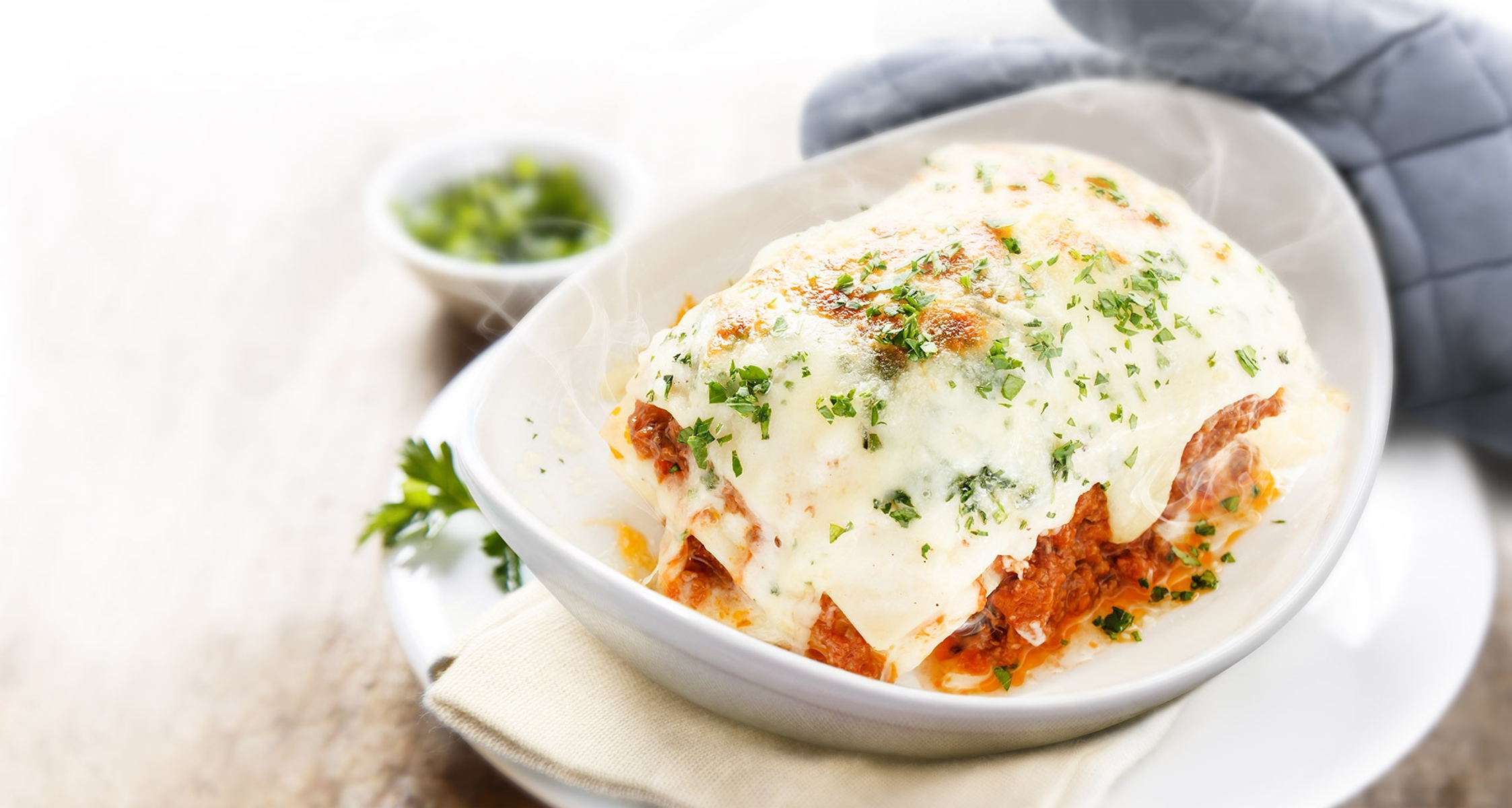 Lasagna al forno in un piatto ovale bianco con sfondo sfocato.