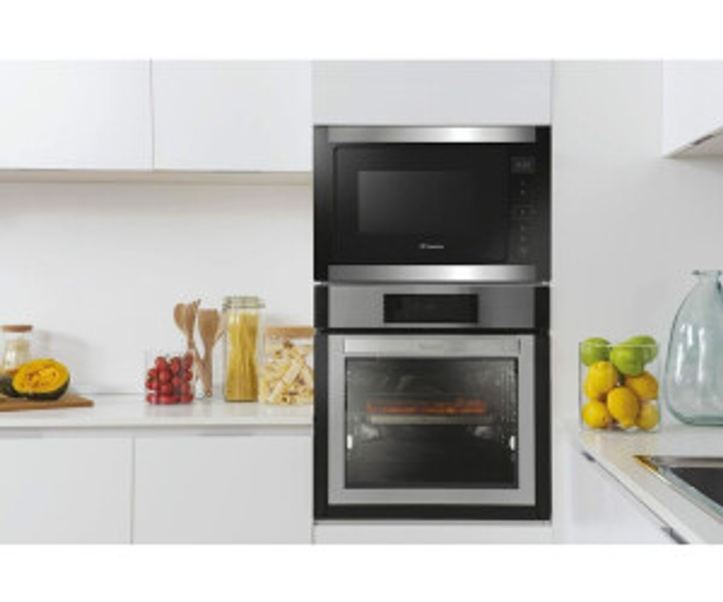 Microonde e forno a incasso. Armadietti e piano cucina con frutta e barattoli visibili.