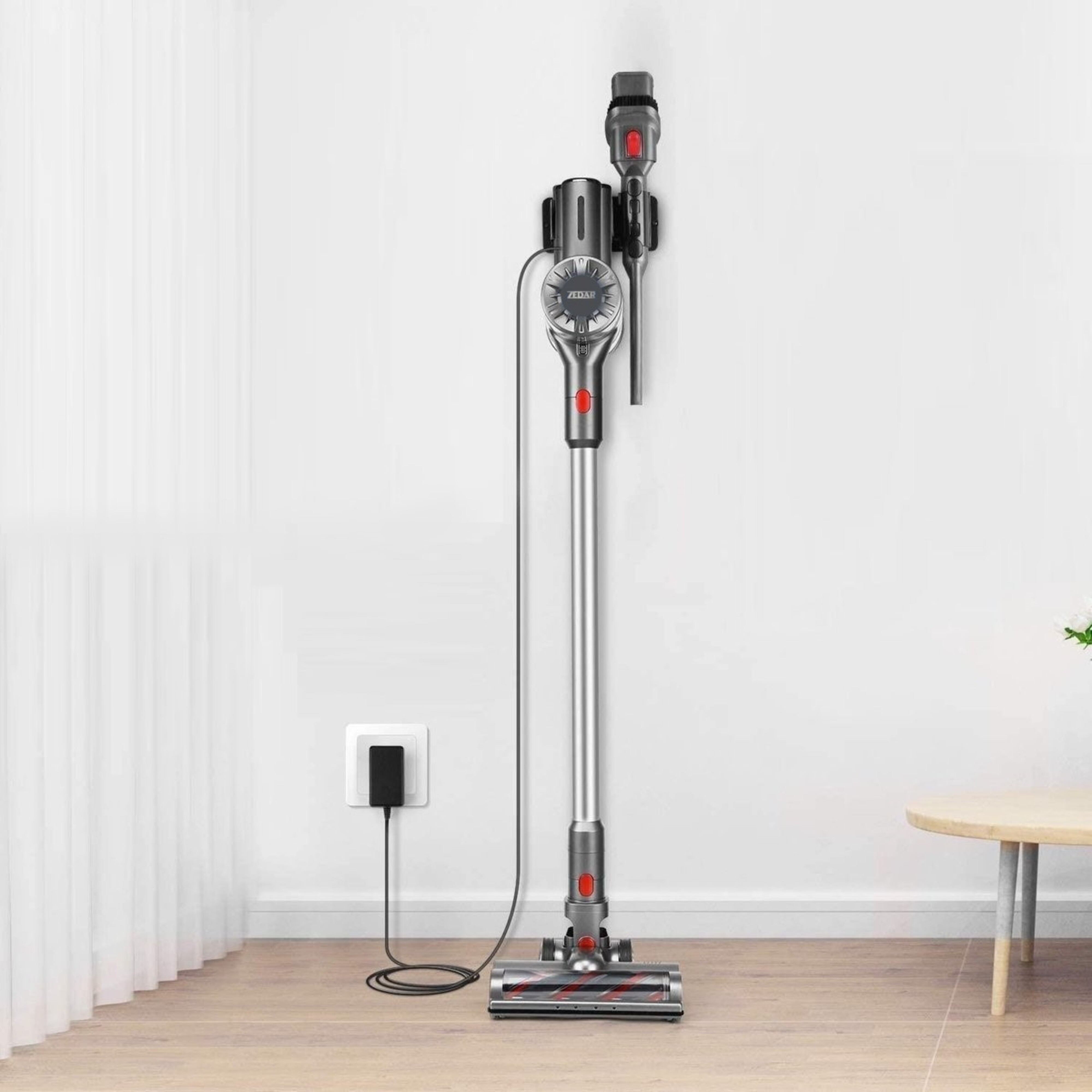 A silver and red cordless vacuum cleaner is mounted on a white wall. A power outlet is on the wall.