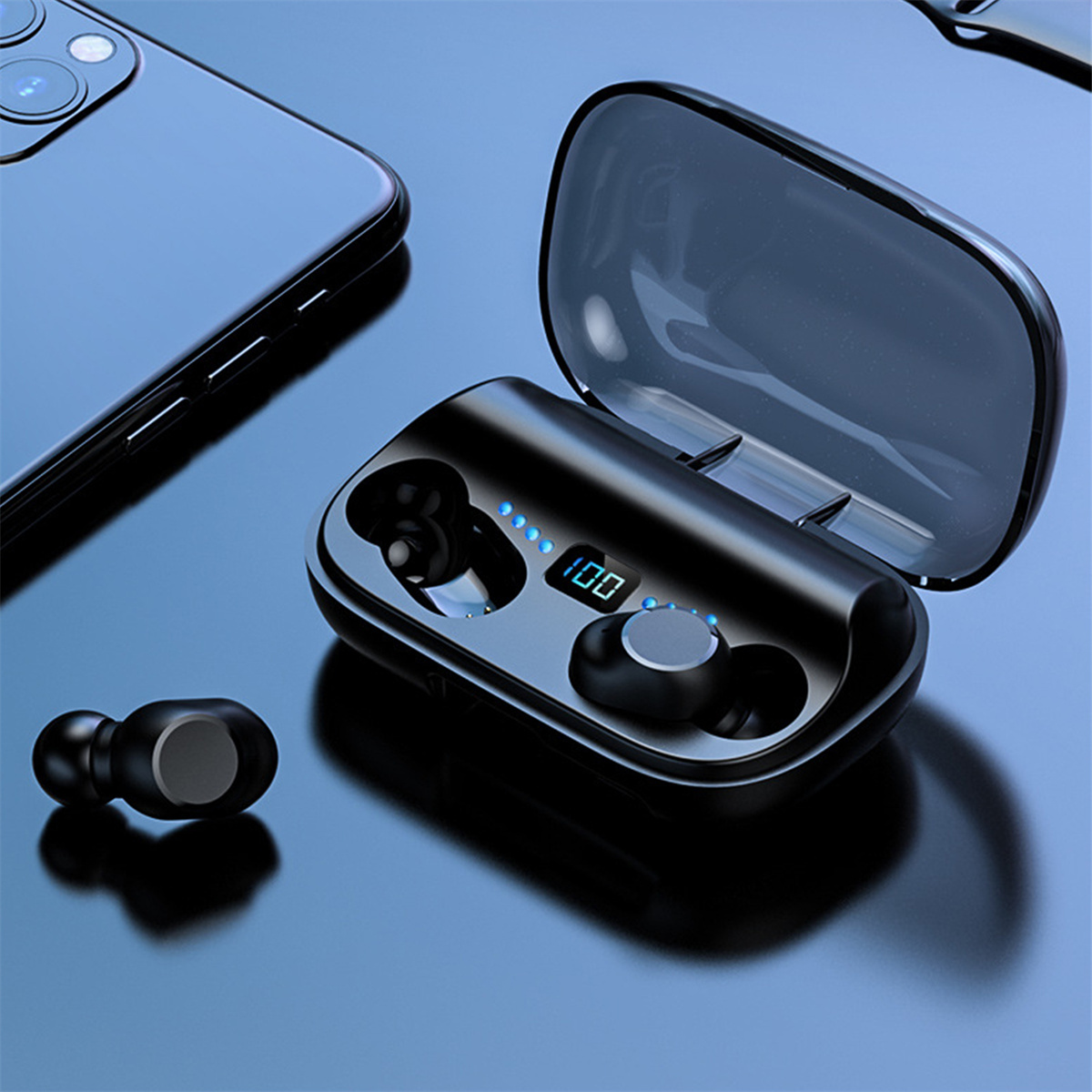 Schwarze Ohrhörer in einem Ladecase, neben einem Telefon auf reflektierender blauer Oberfläche.