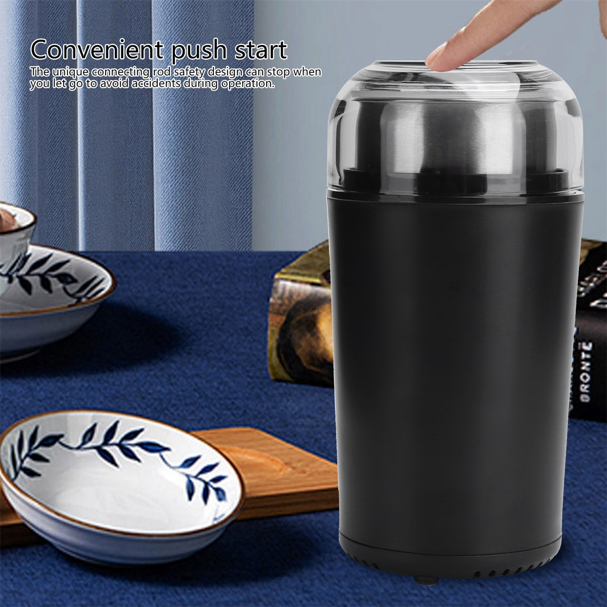 Schwarze Kaffeemühle mit einem Finger, der auf den Deckel drückt, mit Tischhintergrund.