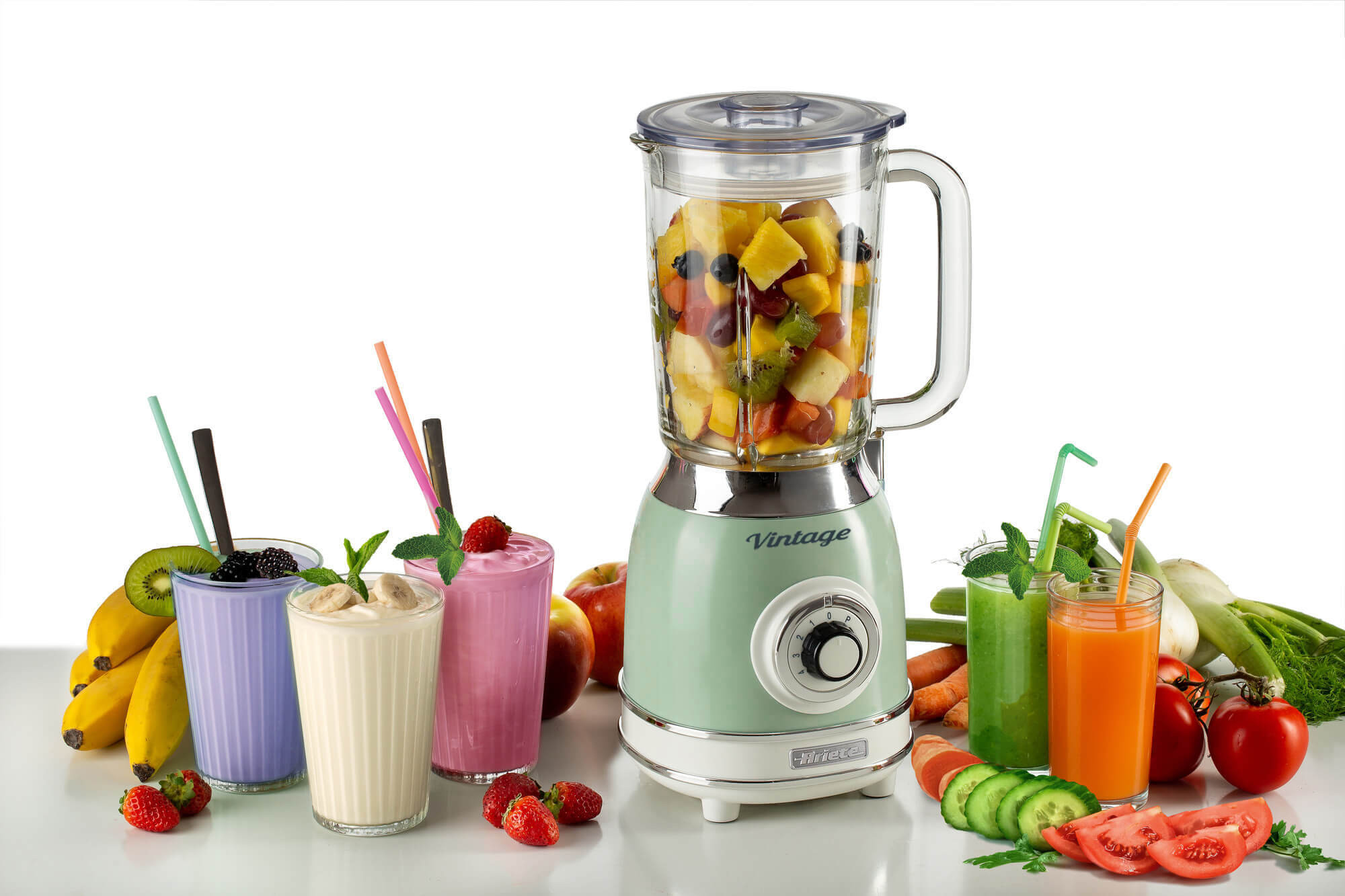 Een blender met fruit en smoothies. Fruit is op tafel rond de blender gerangschikt.