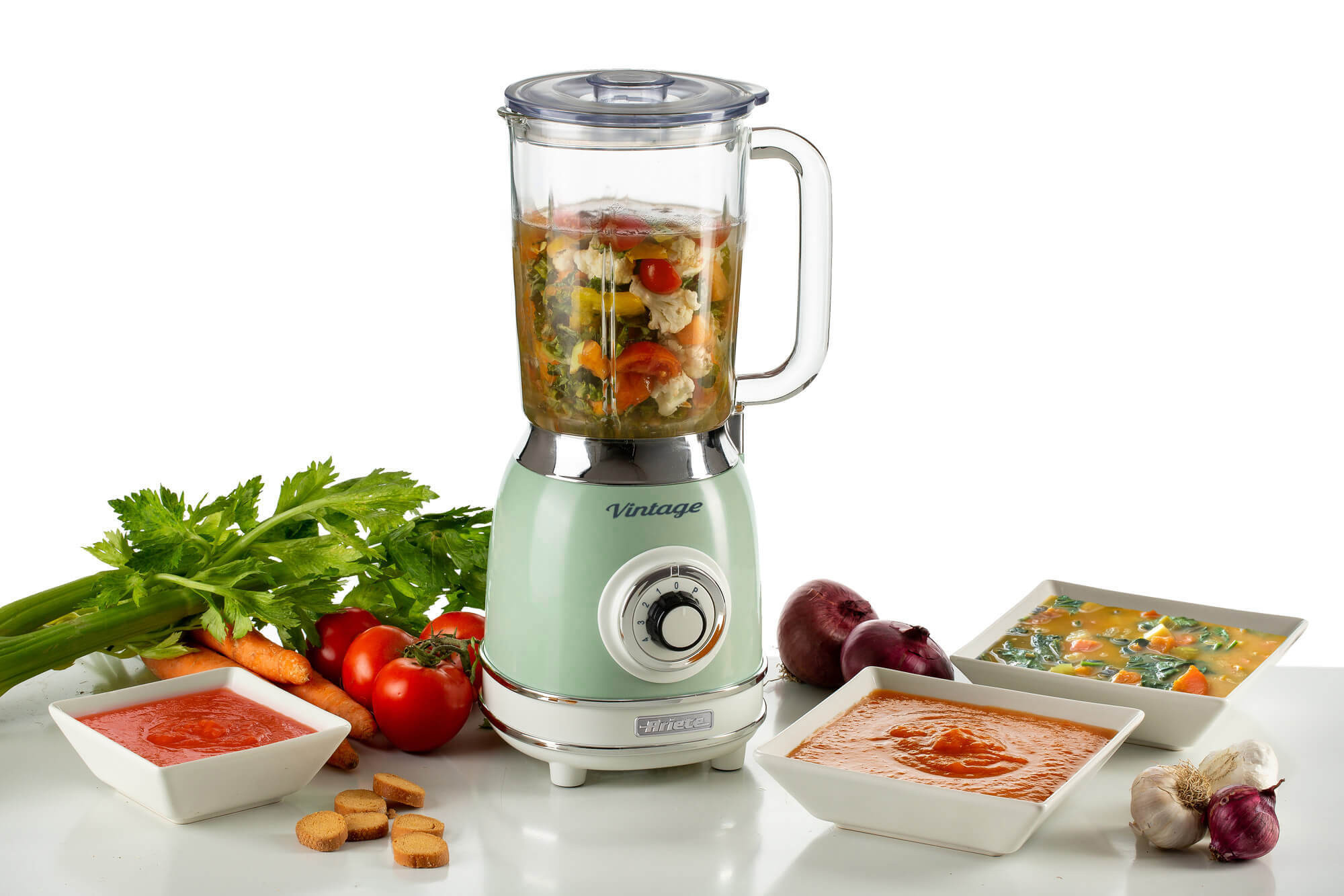 Blender met groenten, bereide soep in kommen en ingrediënten op tafel.