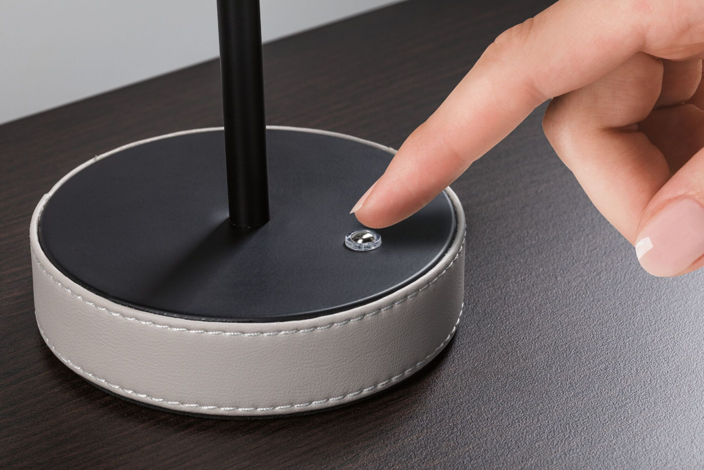 Dłoń dotyka przycisku na podstawie lampy na ciemnej powierzchni.